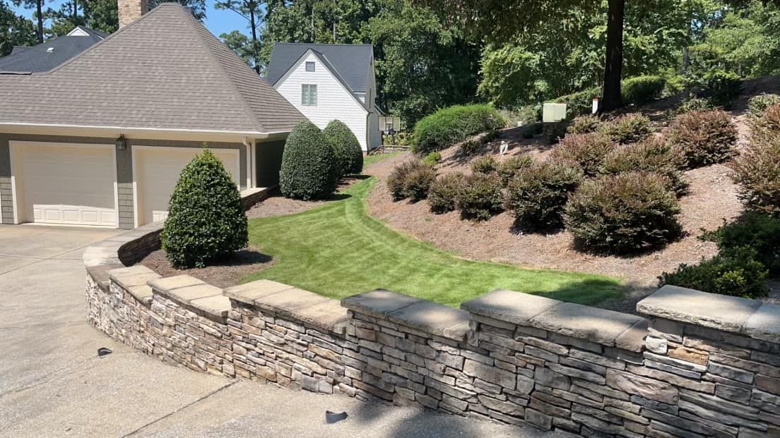 A stone wall surrounds a lush green lawn in front of a house.