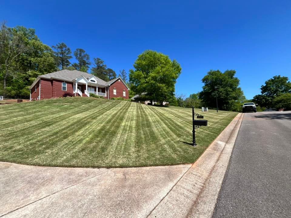 A large brick house with a lush green lawn and a mailbox on the side of the road.