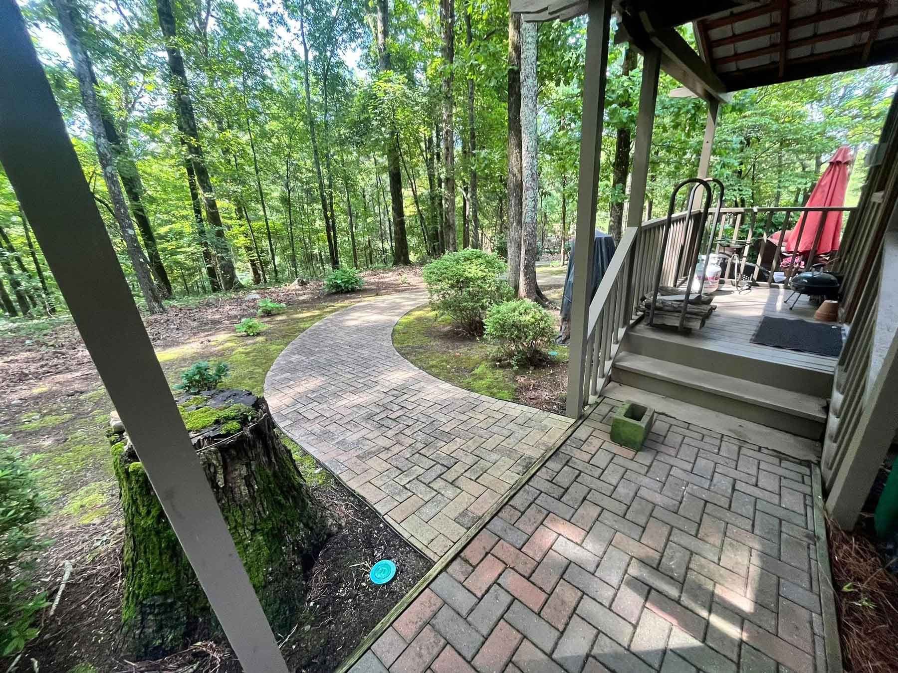 A brick walkway leading to a porch in the woods.