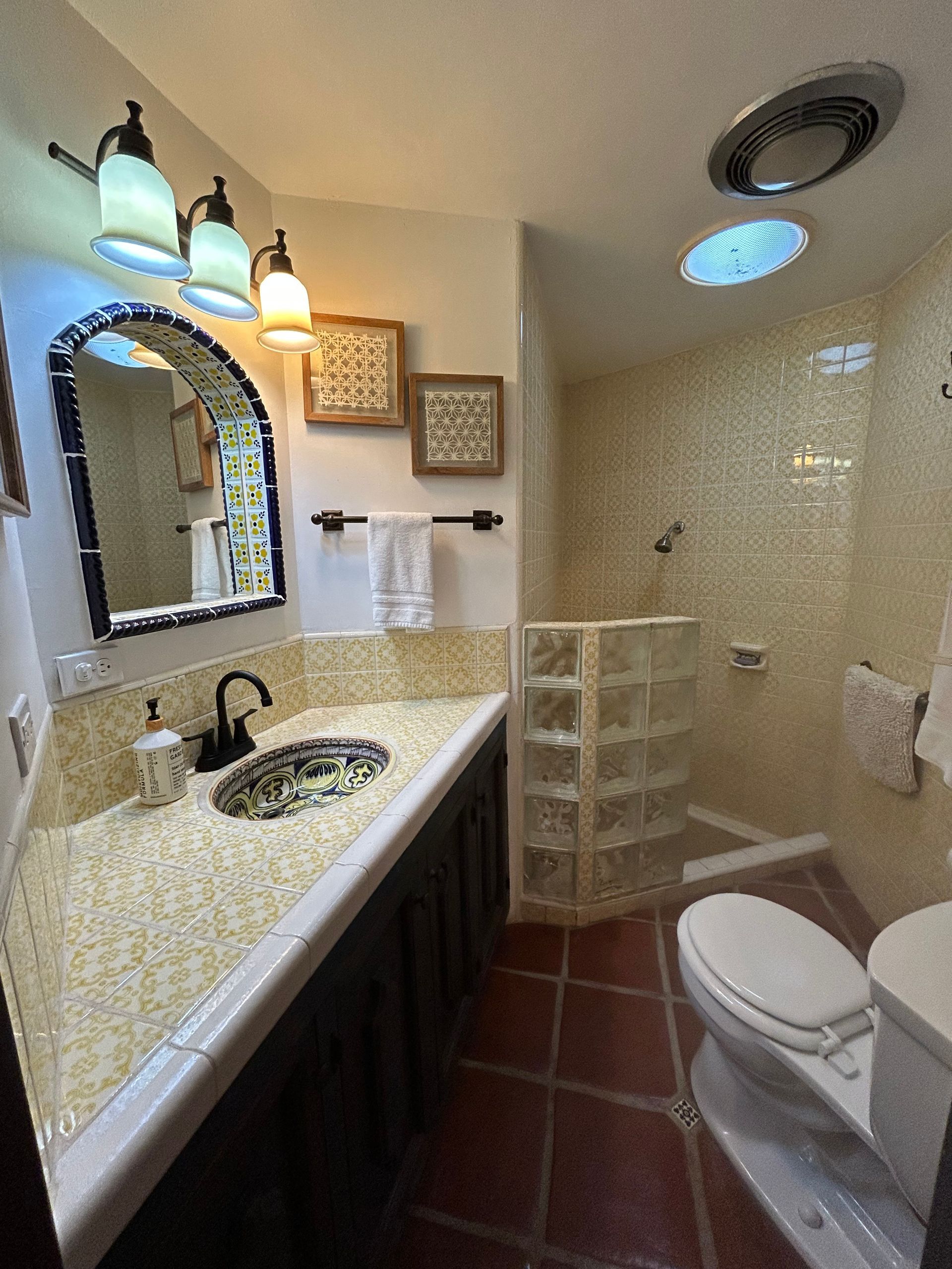 Bathroom with yellow Spanish tile, a shower, pretty yellow and blue tile sink and mirror.