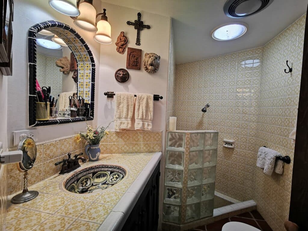 Bathroom with yellow Spanish tile, a shower, pretty yellow and blue tile sink and mirror.
