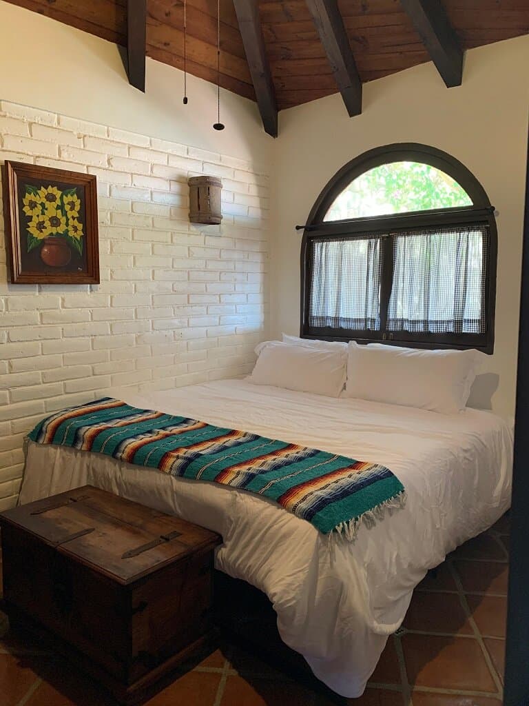 A king-size bed and painting of sunflowers. Tile floor. Window above the bed.