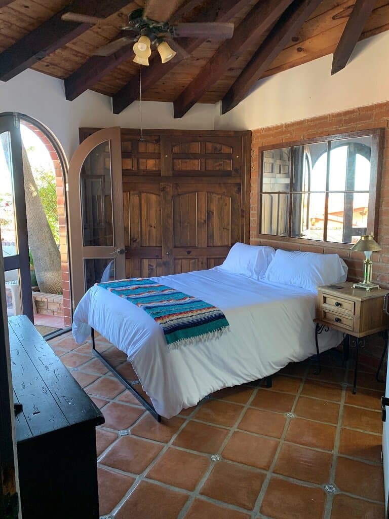 Queen size bed with a white comforter, tile floor, colorful blanket, and French doors opening onto the patio