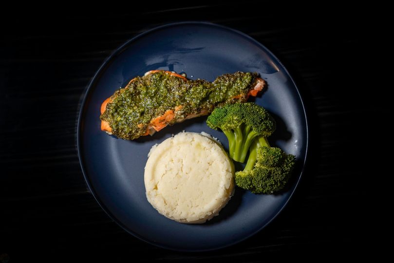 A blue plate topped with a piece of salmon , broccoli and mashed potatoes.