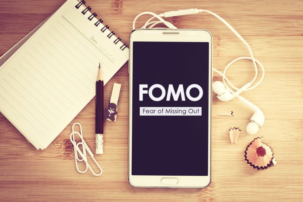 Smart phone with the words 'FOMO fear of missing out' displayed on the screen