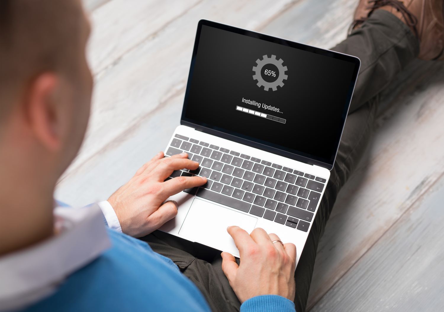 Man sitting with open laptop that has  the words 'installing updates' on the screen