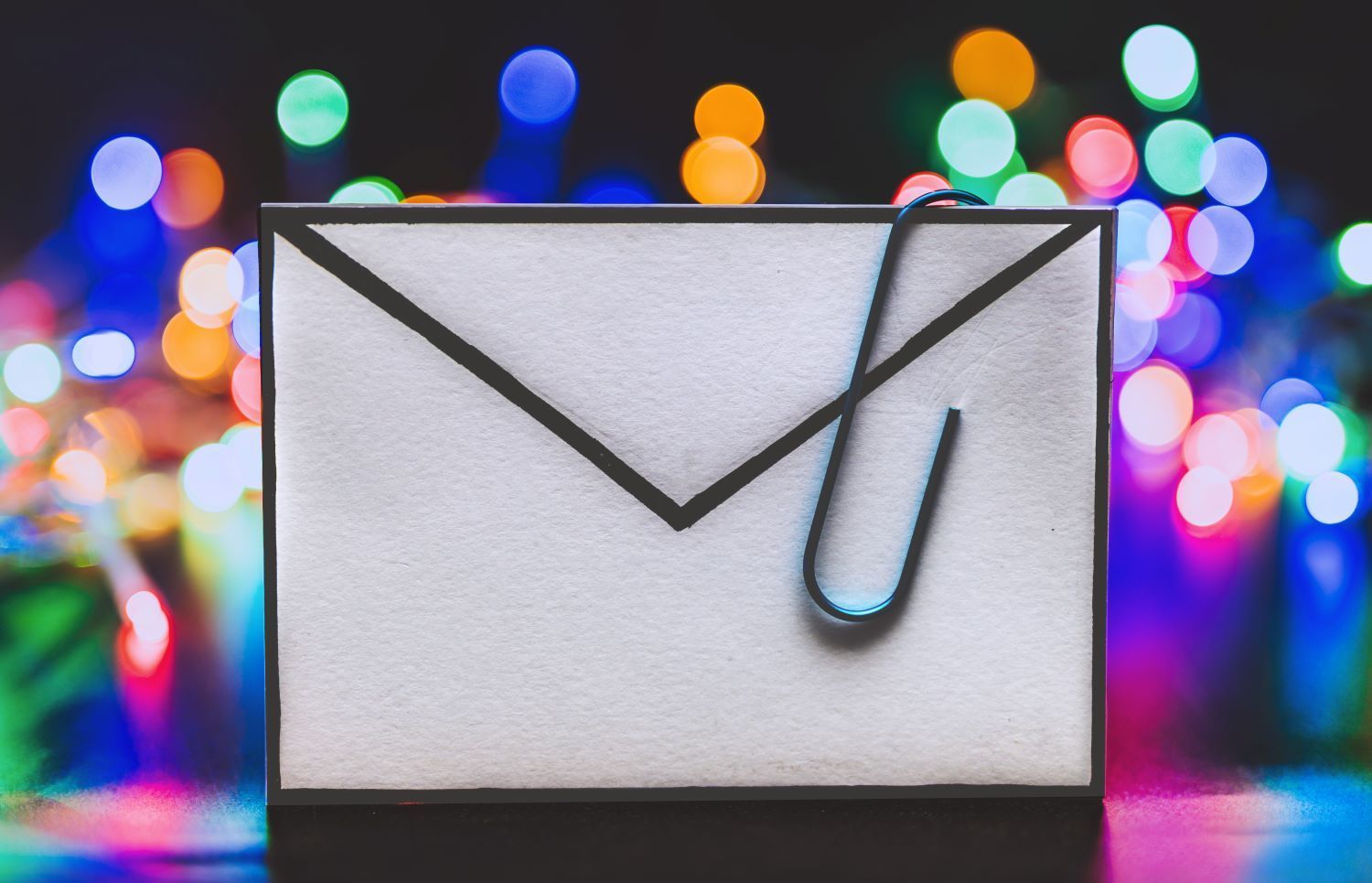 Picture of an envelope with a giant paperclip attached, and colourful lights in the background