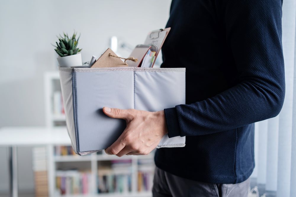 Man in business suit walking out of an office carrying a box with all their desk items in