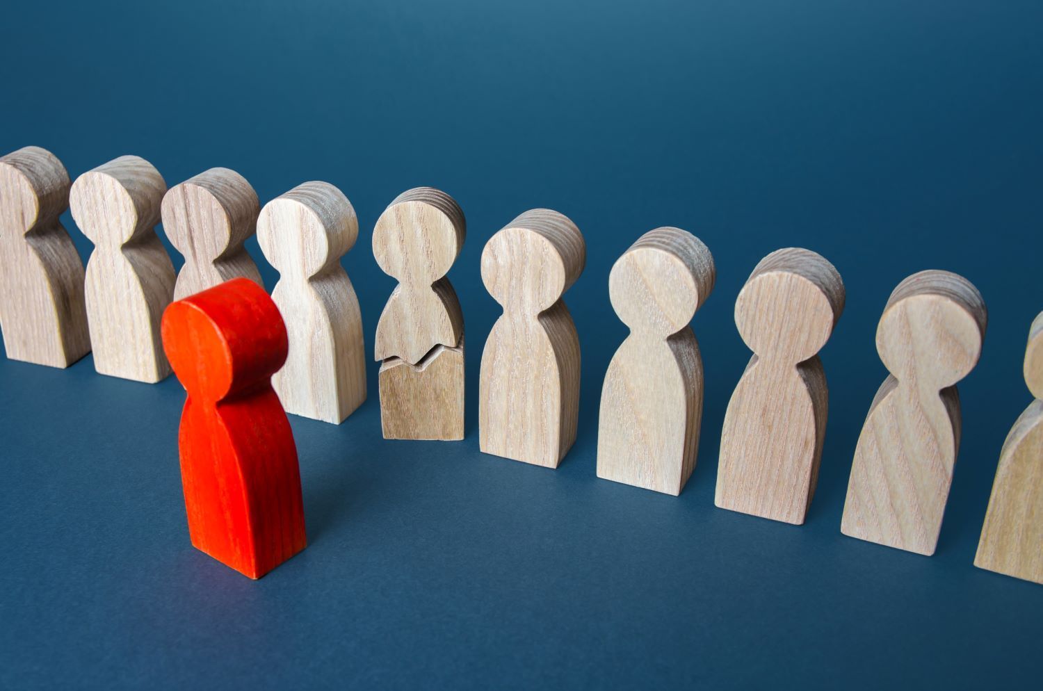 Row of wooden people ornaments with one cracked through the middle and a red wooden person ornament 