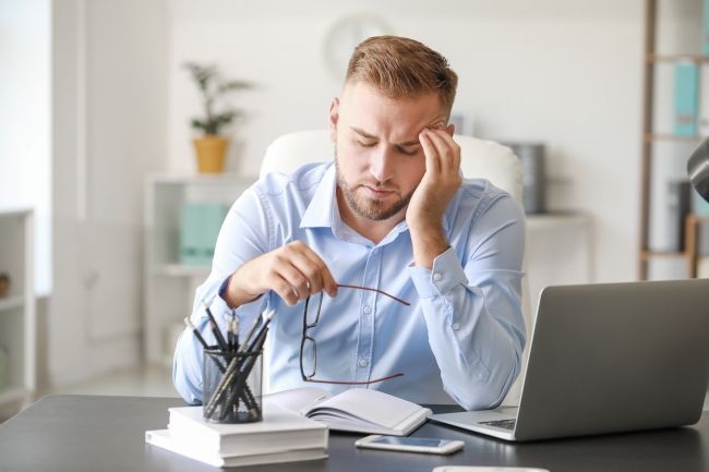 Business man rubbing his head, sitting in front of his laptop