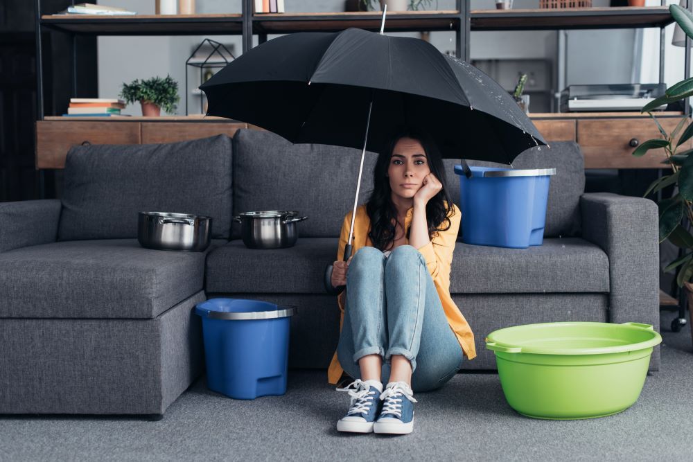 Woman sitting indoors under an umbrella as there is a leak in the roof dripping down