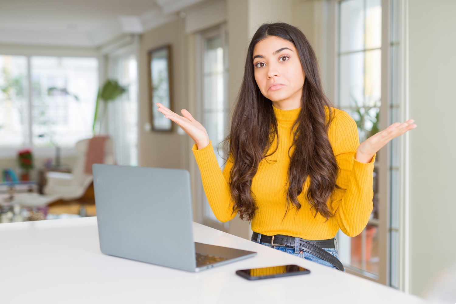 Woman sitting in front of a laptop with her arms in the air shrugging