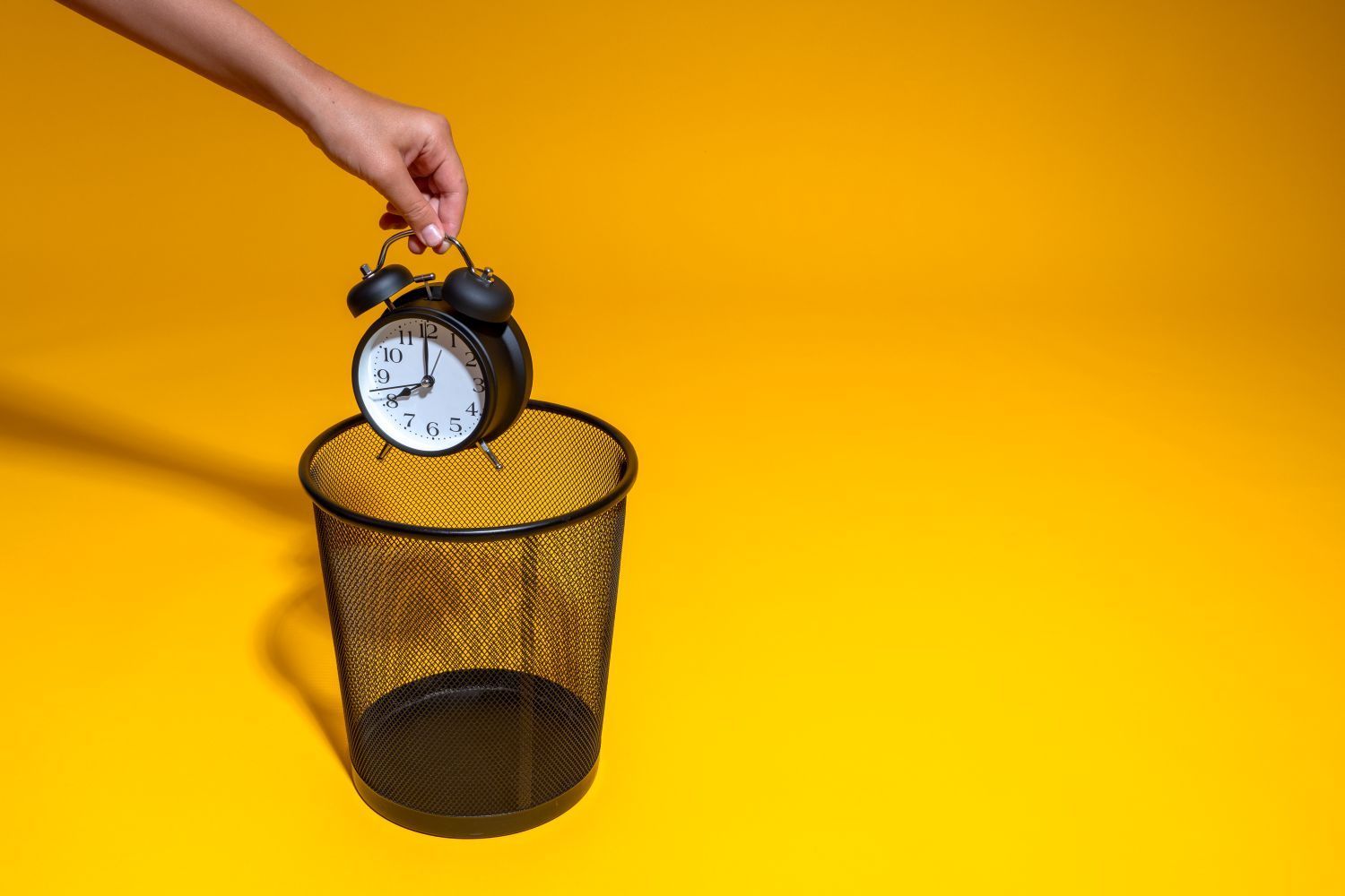 Someone dropping an alarm clock into a waste paper bin