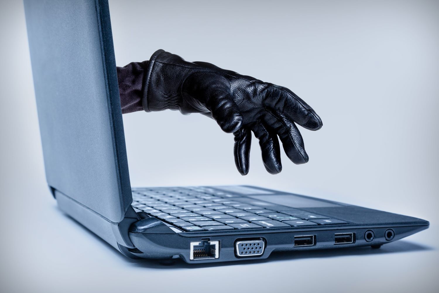 Open laptop with a hand in a black leather glove coming out the screen and reaching to the keyboard