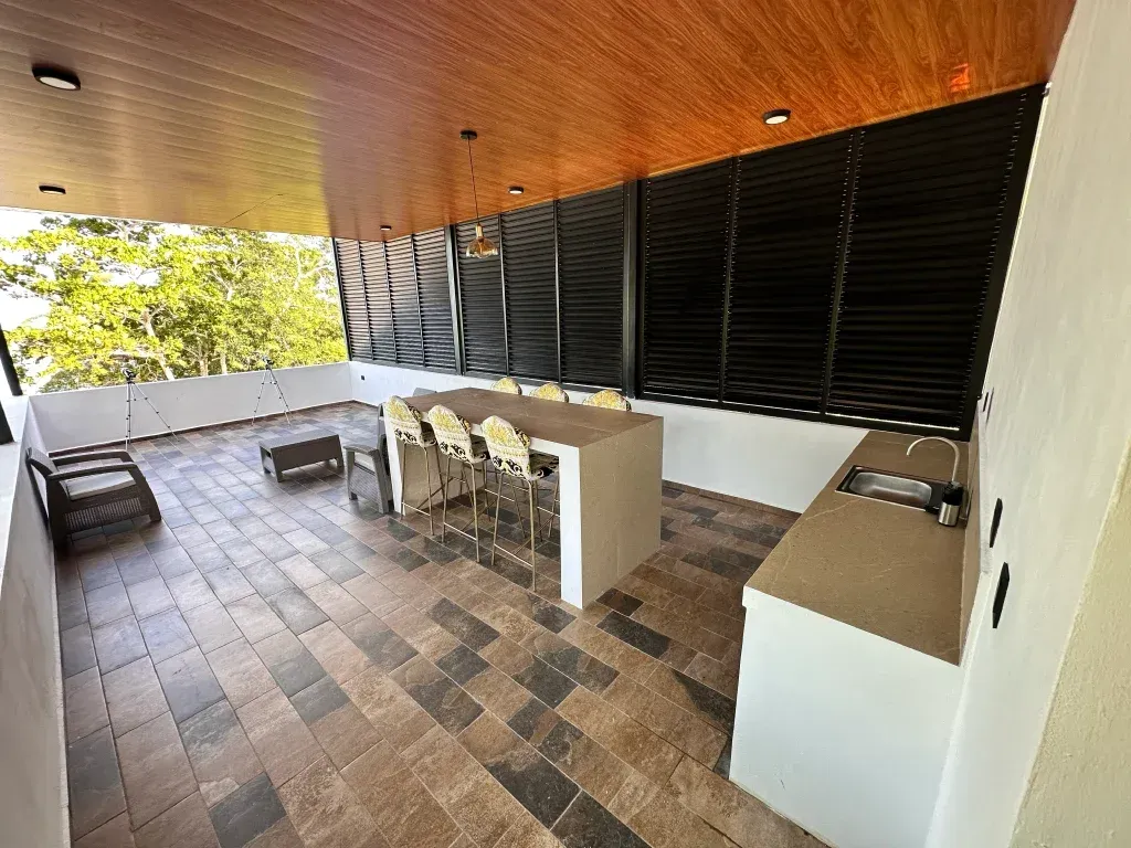 Patio exterior con bar, asientos y vistas; suelo de baldosas marrones y grises, techo marrón.