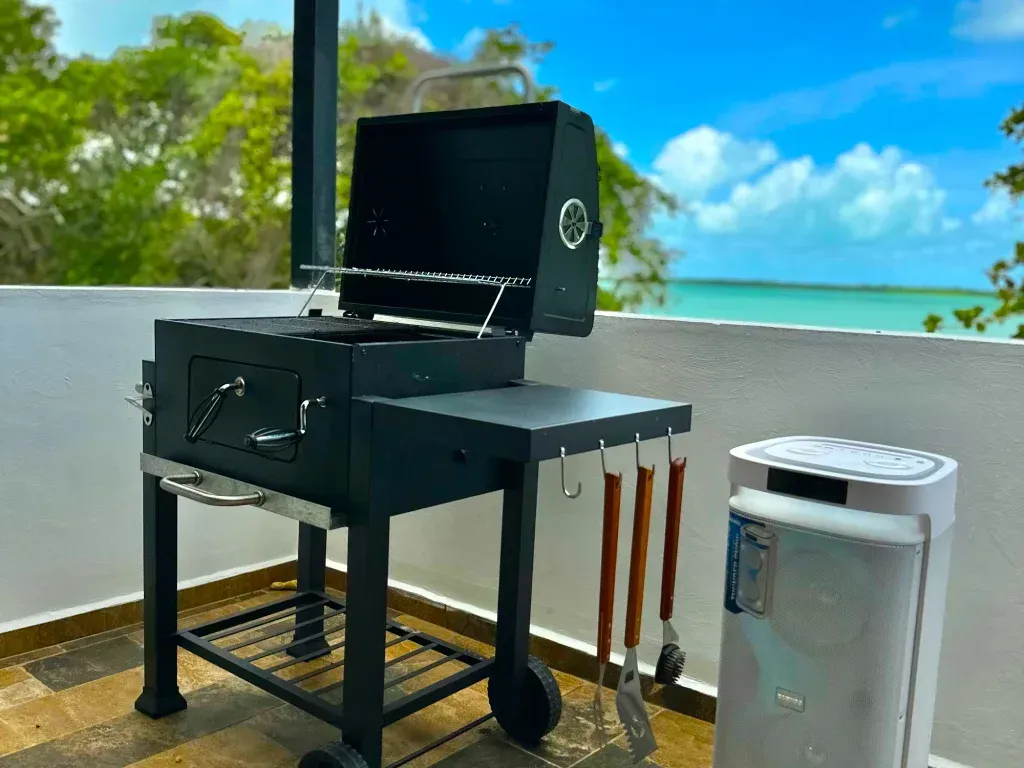 Parrilla de carbón negro en un patio con vistas al océano y cielo azul.