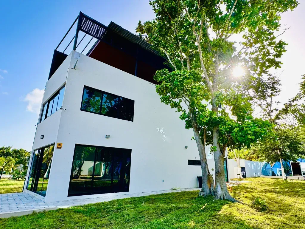 Modern white building with black framed windows, rooftop deck, and green lawn.