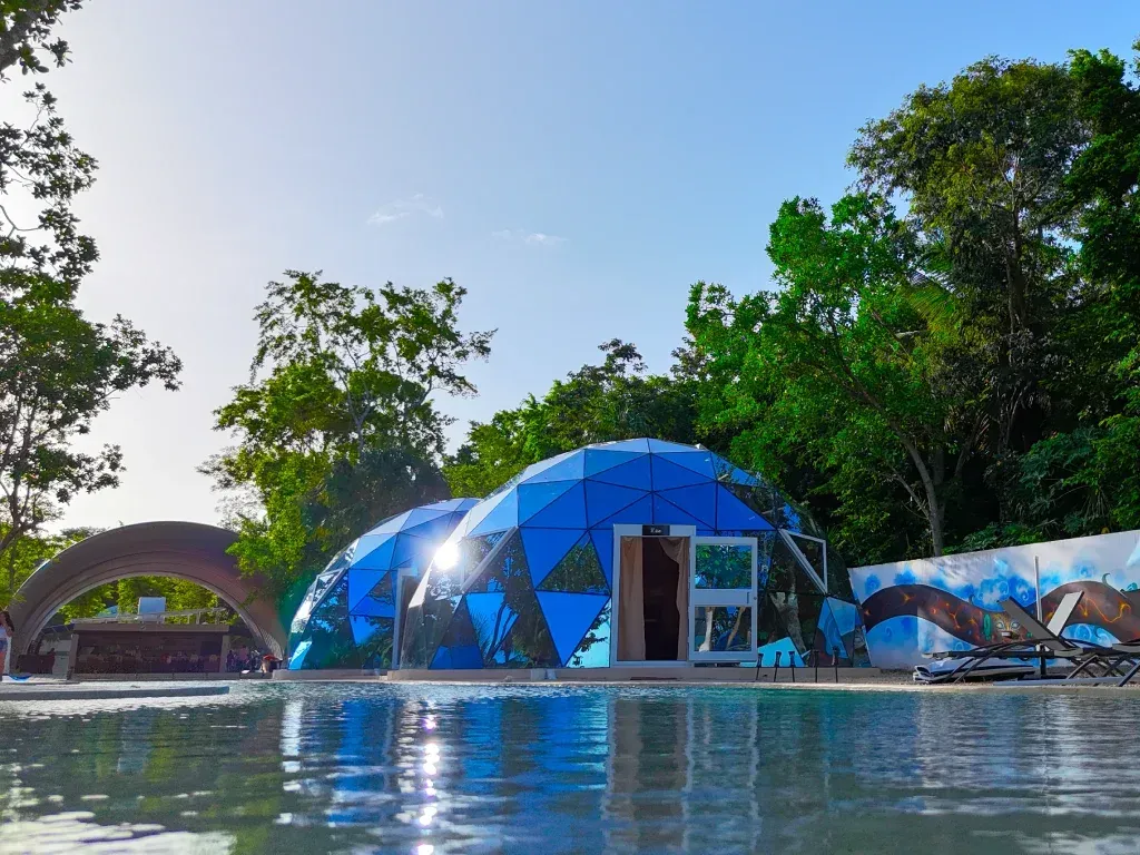 Two blue geodesic dome structures next to a pool in a tropical setting.