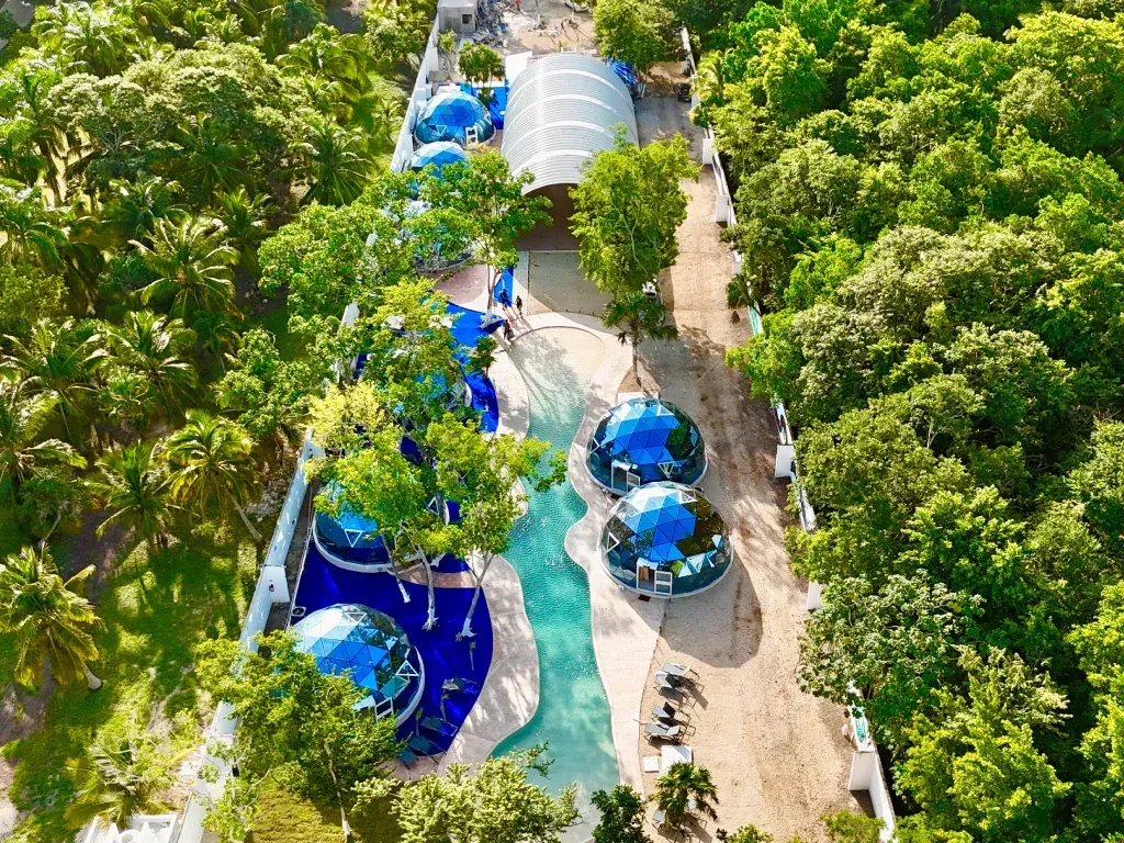 Vista aérea de un complejo turístico con edificios azules en forma de cúpula, una piscina y exuberantes árboles verdes.