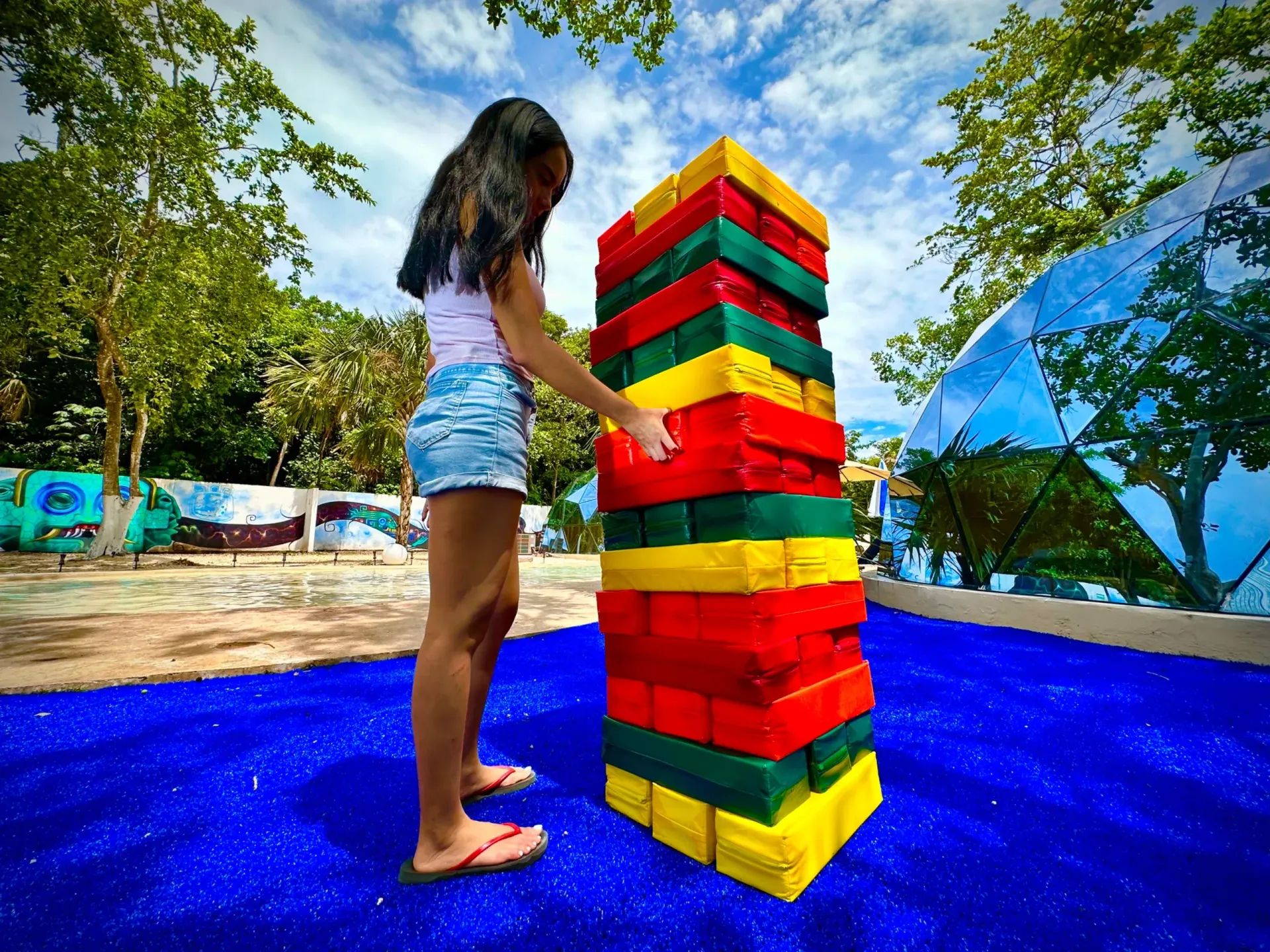 Una persona jugando al Jenga con bloques grandes y coloridos al aire libre sobre una superficie azul.
