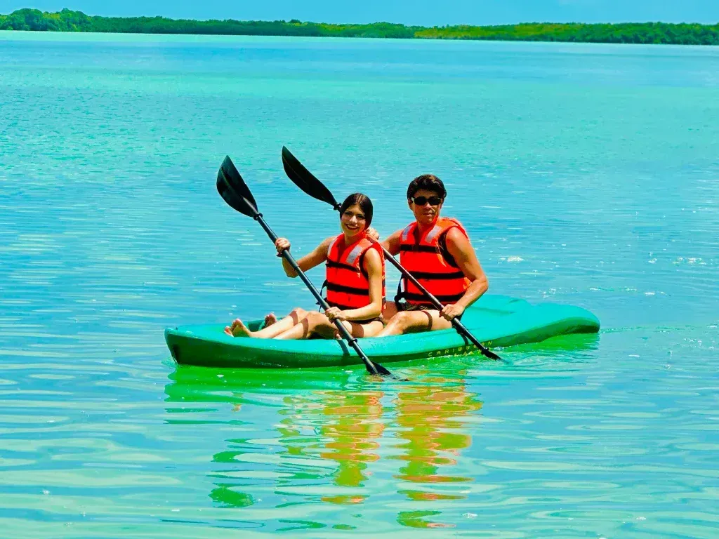 Dos personas con chalecos salvavidas naranjas practicando kayak en aguas turquesas.