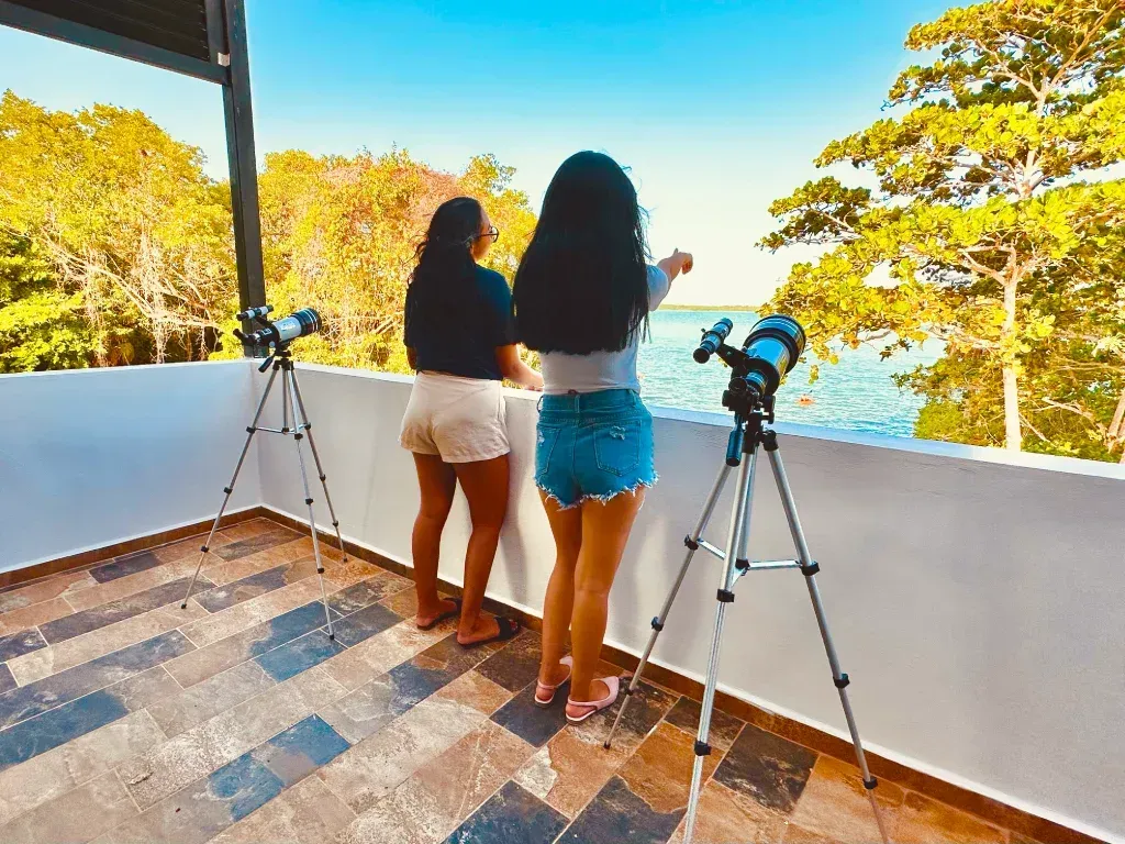 Dos personas observando el agua a través de telescopios en una terraza, en un día soleado.