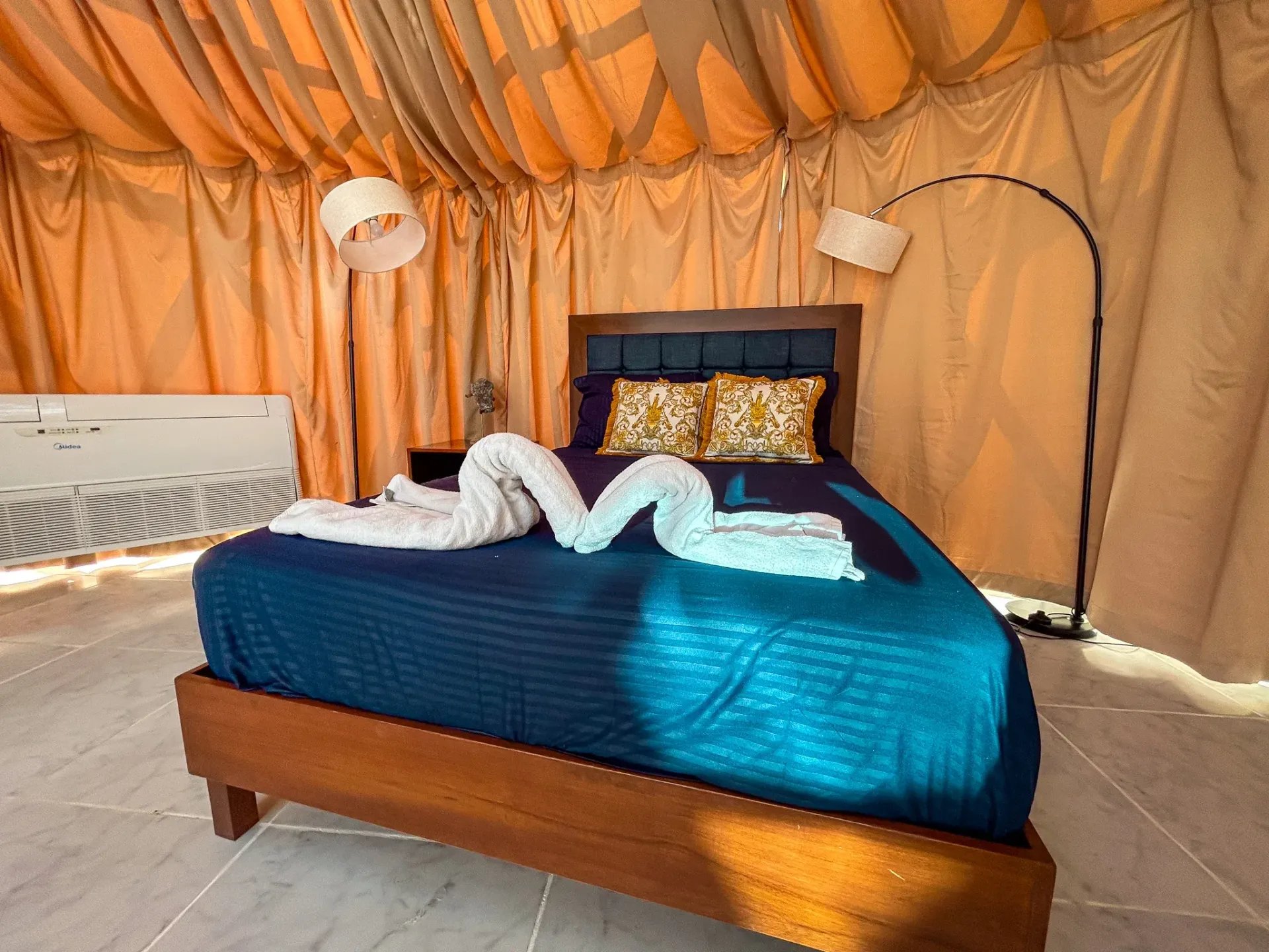 Interior del dormitorio: cama con decoración de toalla en forma de cisne, ropa de cama color azuly  dos lámparas.