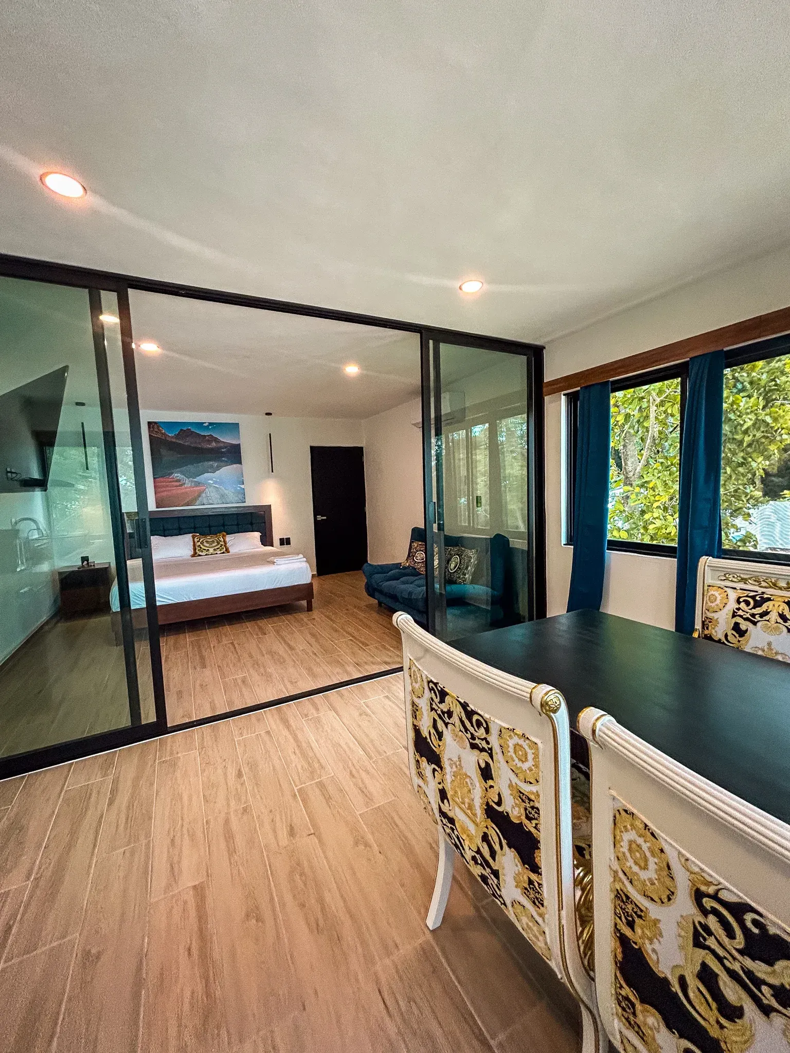 Vista interior: dormitorio con puertas corredizas de vidrio, comedor con sillas ornamentadas y un pequeño sofá.