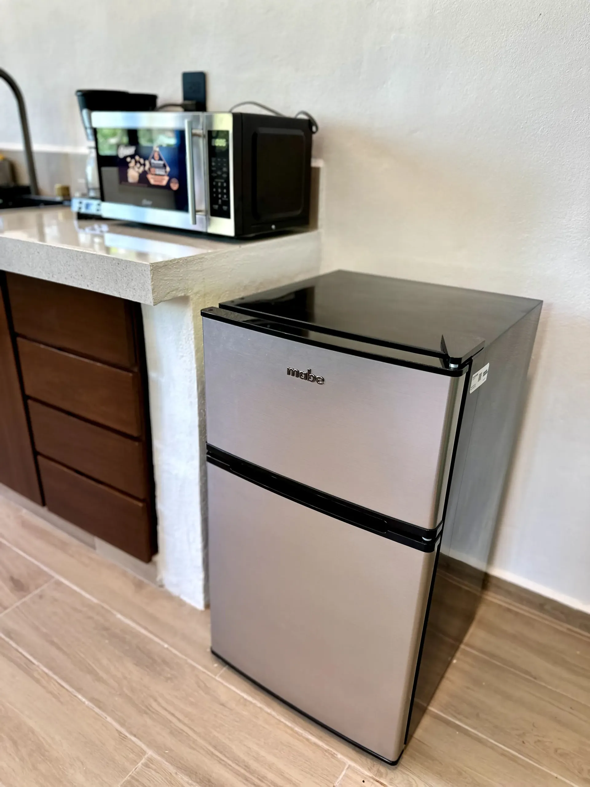 Mininevera, microondas y cafetera sobre la encimera de una cocina.