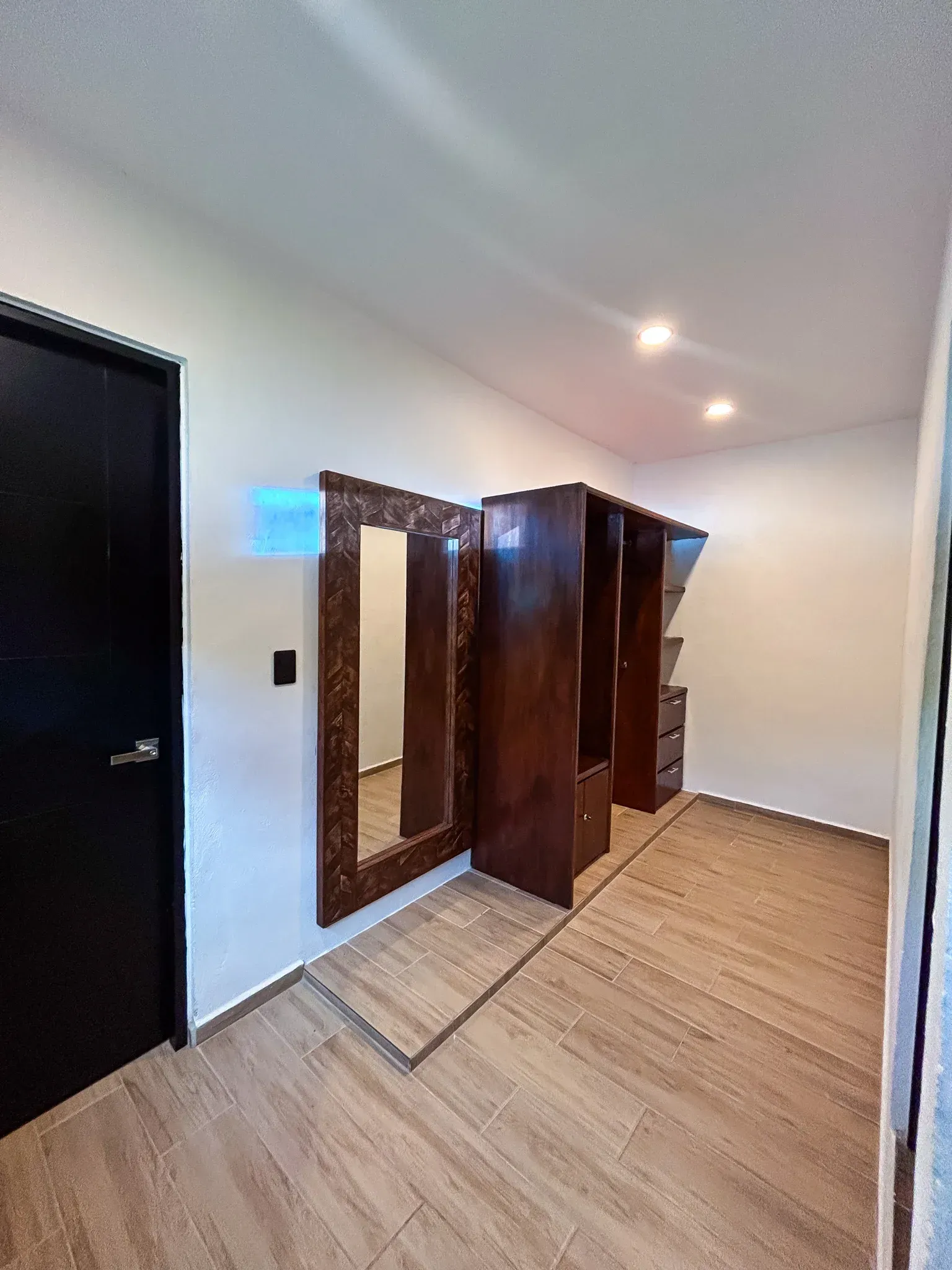 Dormitorio con armarios de madera y un gran espejo. Puerta negra a la izquierda.