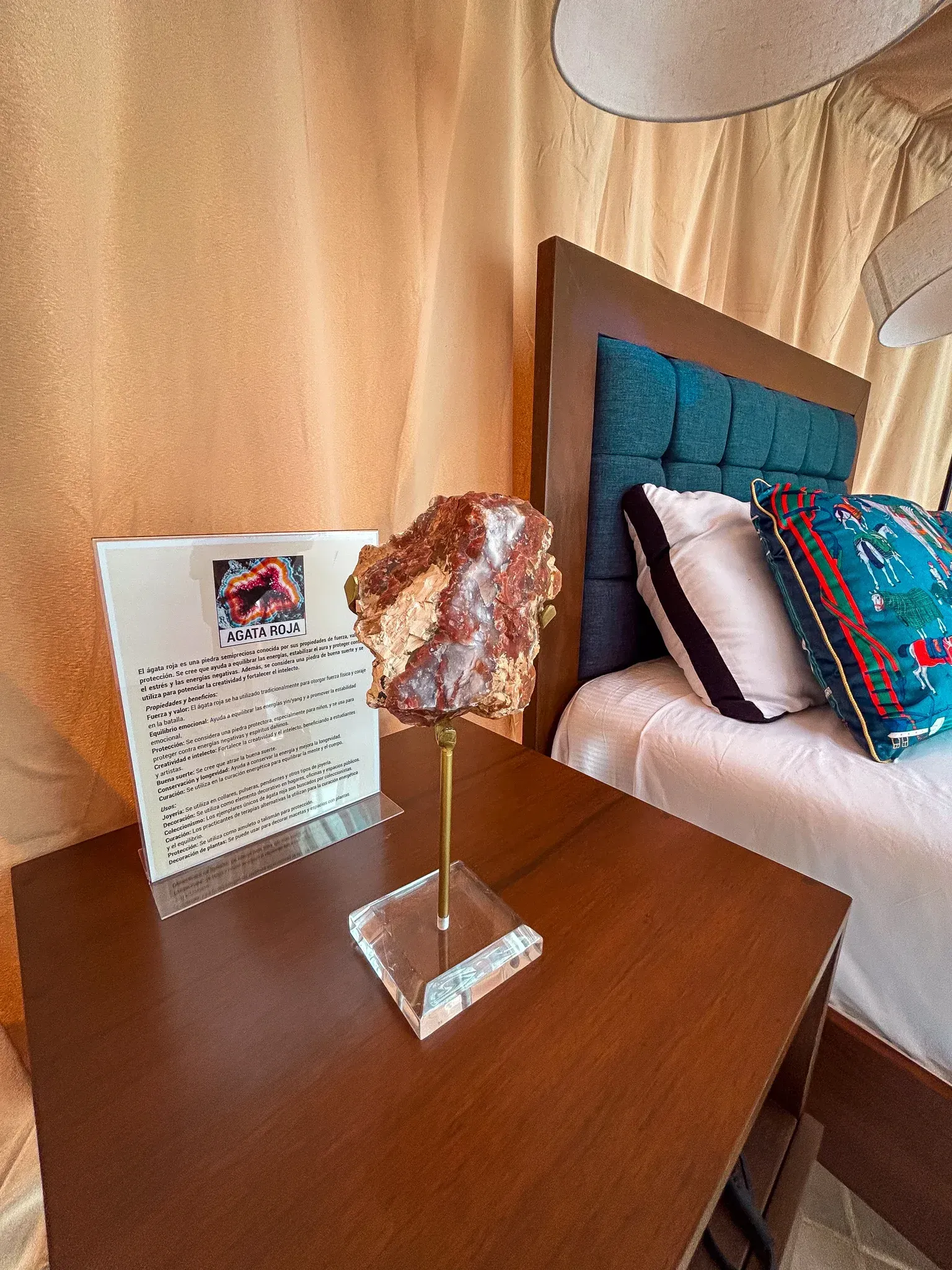 Exhibidor de cristal marrón sobre una mesita de noche junto a una cama con cabecero turquesa y cojines decorativos.