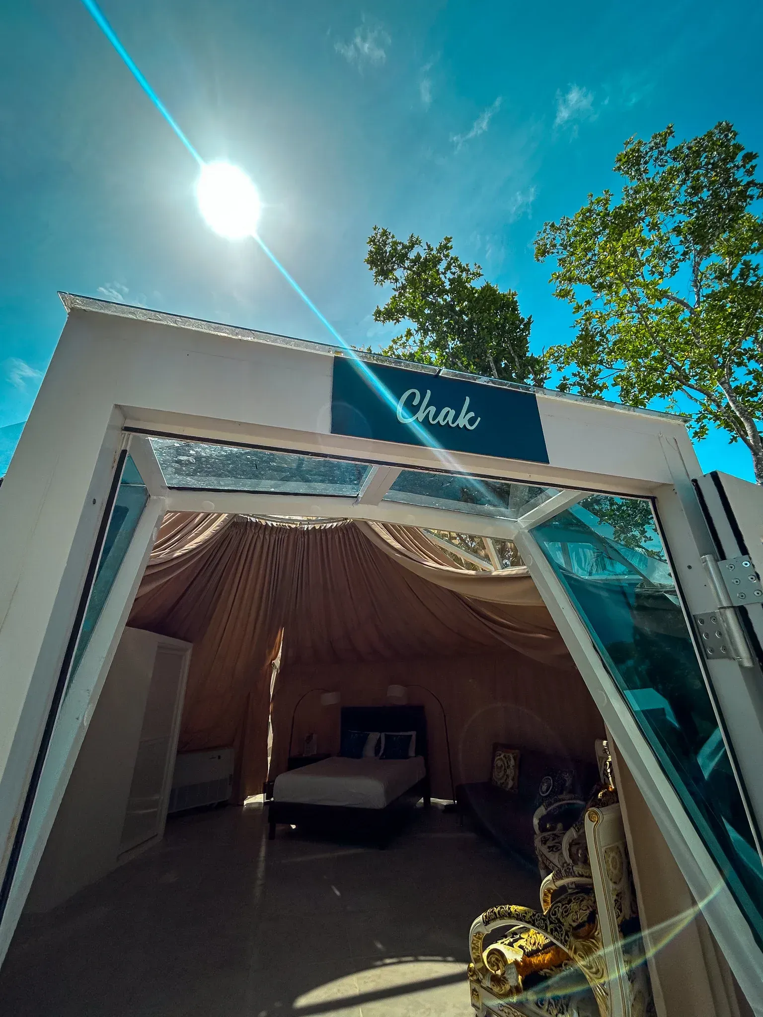 Entrada blanca y de cristal a una estructura tipo tienda de campaña, con una cama visible en el interior,