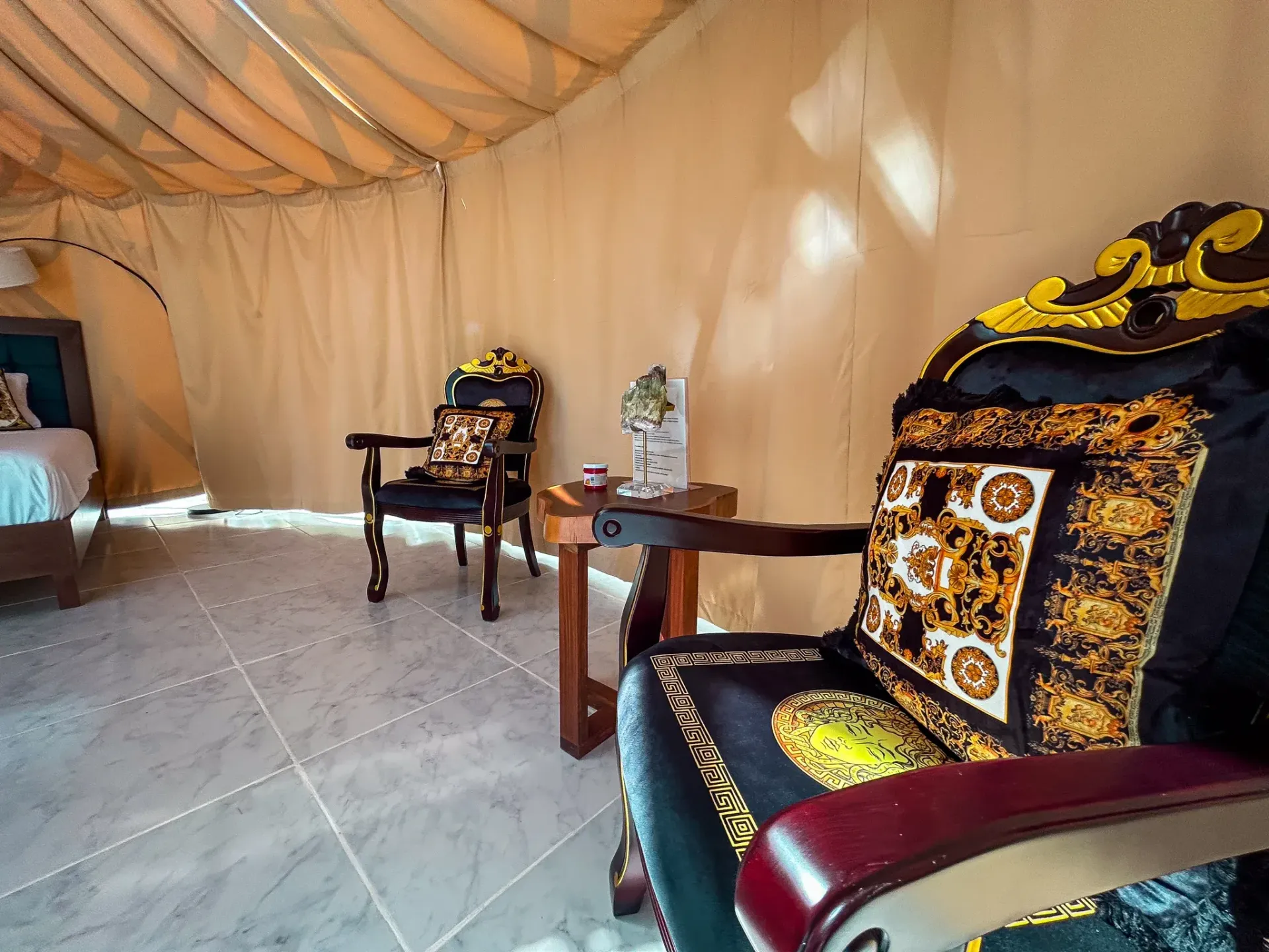 Interior de una tienda de campaña de lujo con dos sillas ornamentadas, una mesita y una cama.