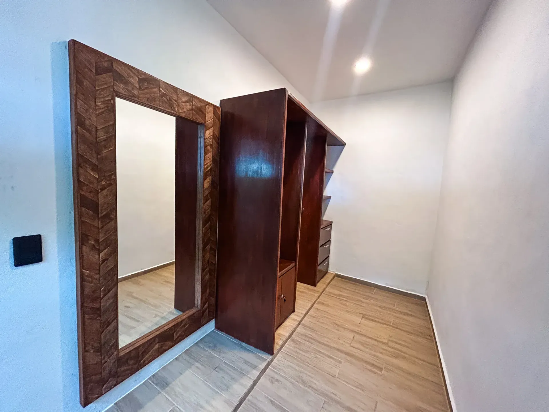 Vestidor con armarios de madera oscura y un gran espejo con marco decorativo. Suelo de madera.
