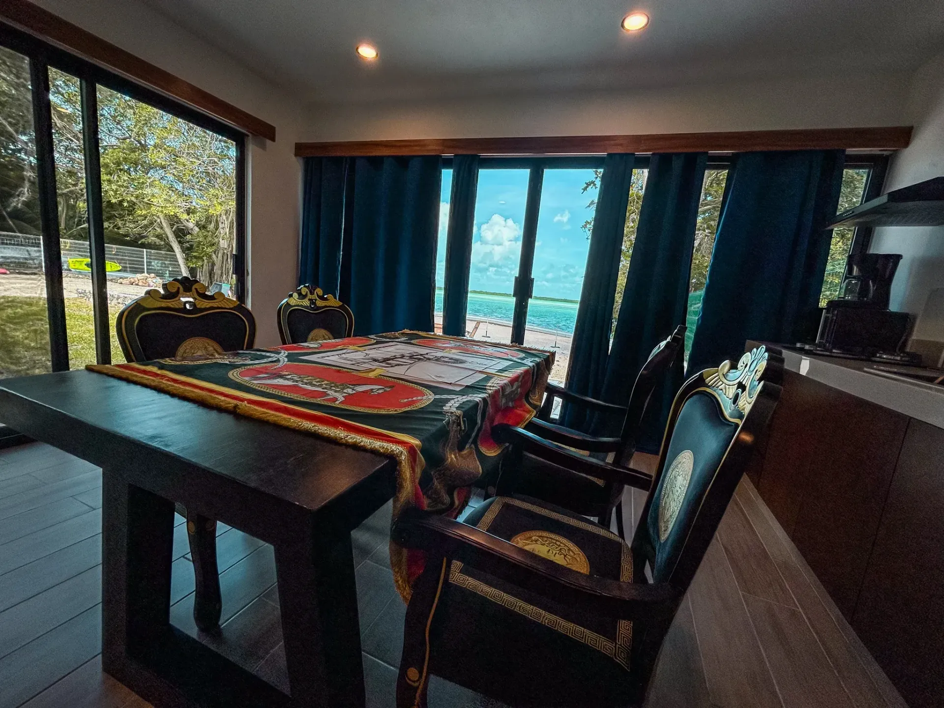 Comedor con mesa y sillas de madera oscura, vista al mar a través de puertas corredizas de vidrio, cortinas azul oscuro.