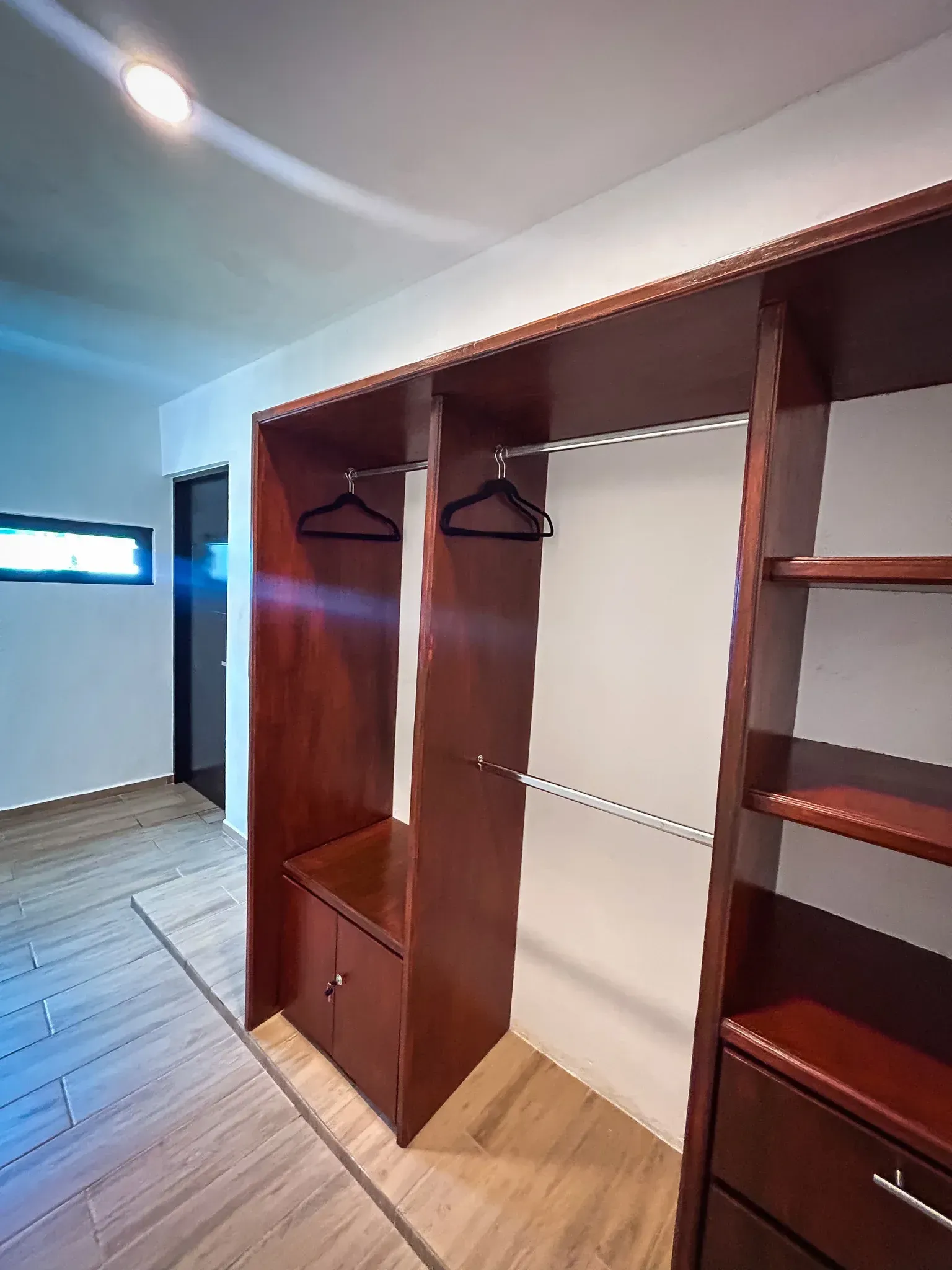 Interior de armario de madera con barras para colgar ropa, estantes y un pequeño armario.