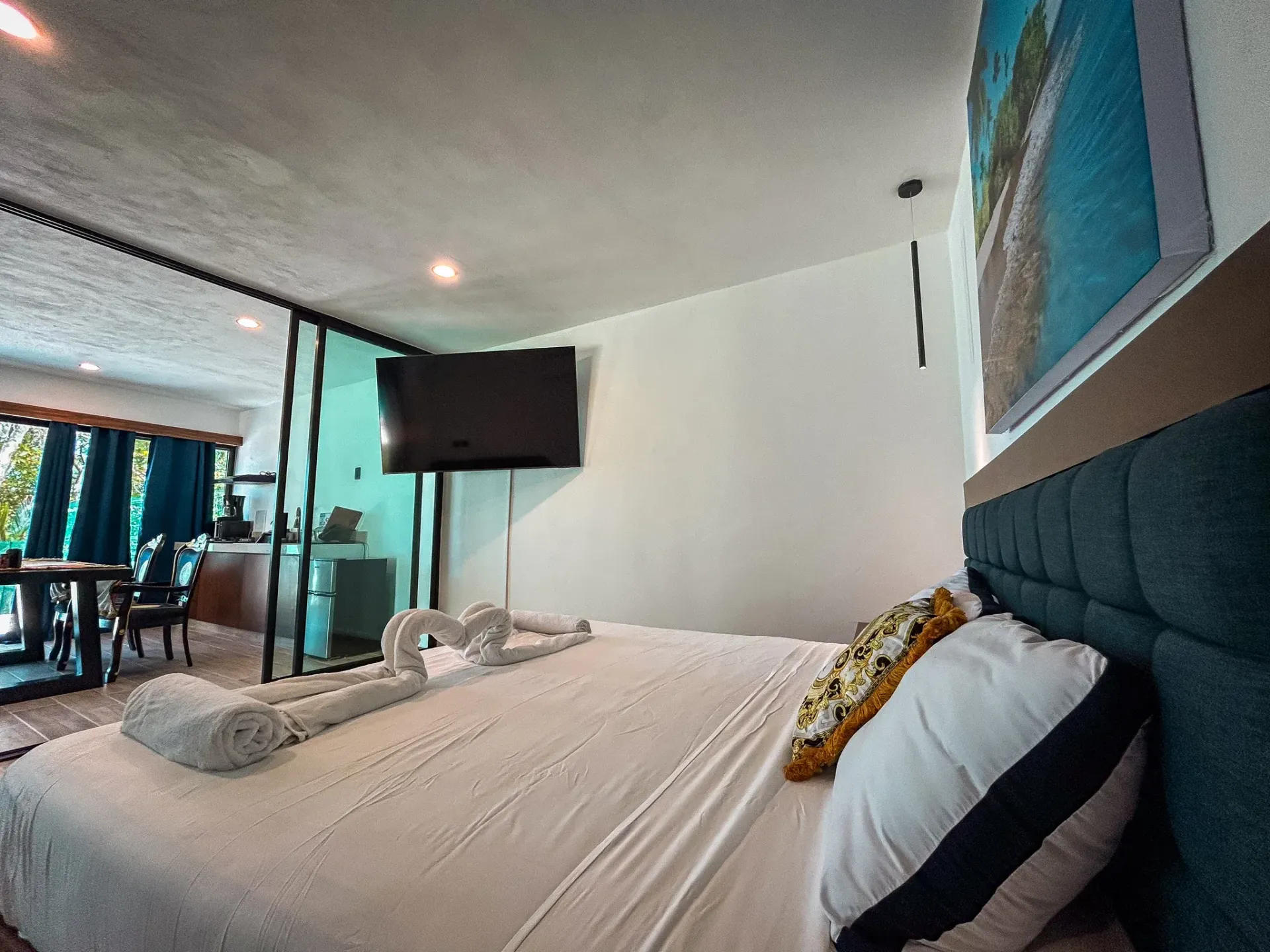 Dormitorio con cama grande, TV y mampara de cristal que comunica con la sala de estar.