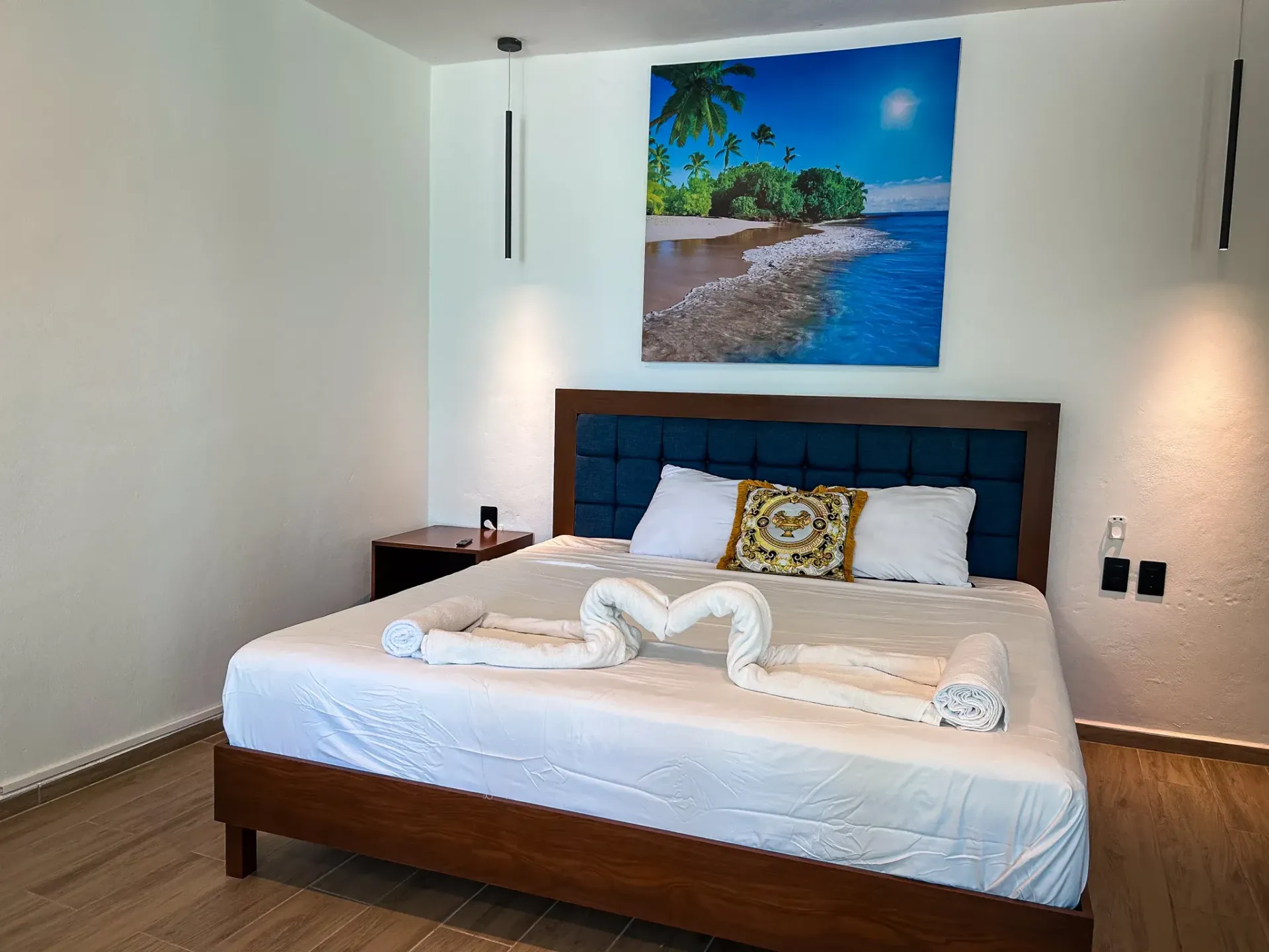 Dormitorio con una cama grande, decorado con cisnes de toalla, debajo de un cuadro de paisaje tropical.