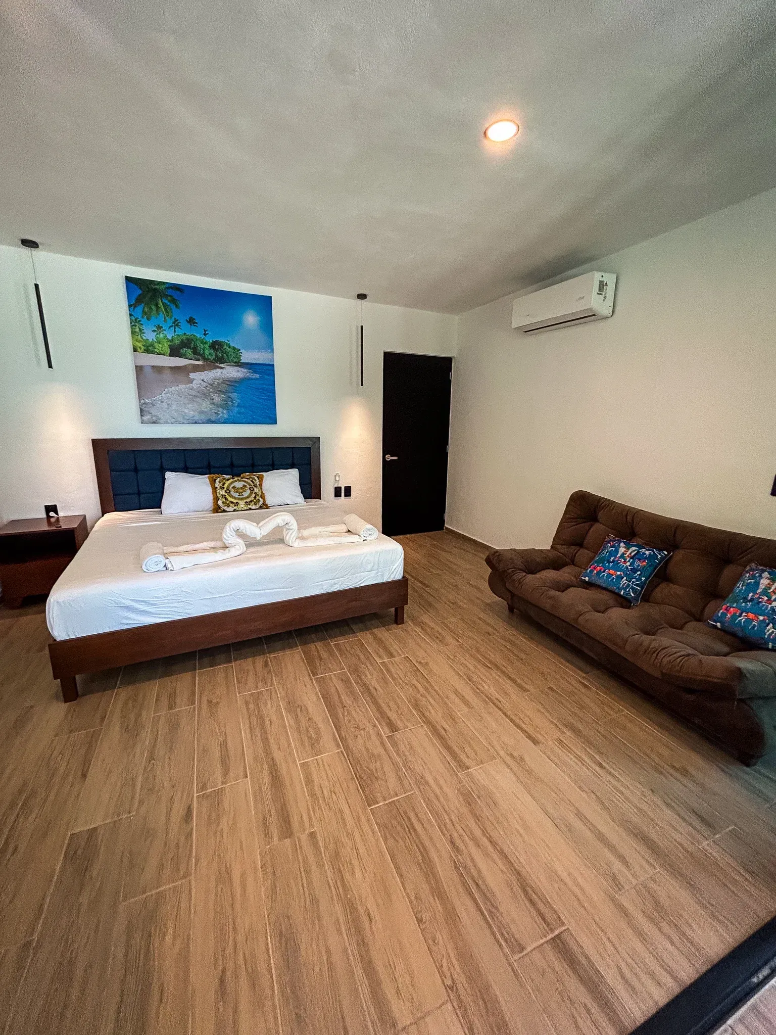 Dormitorio con cama, futón y decoración de pared. Suelo de madera marrón y paredes blancas.