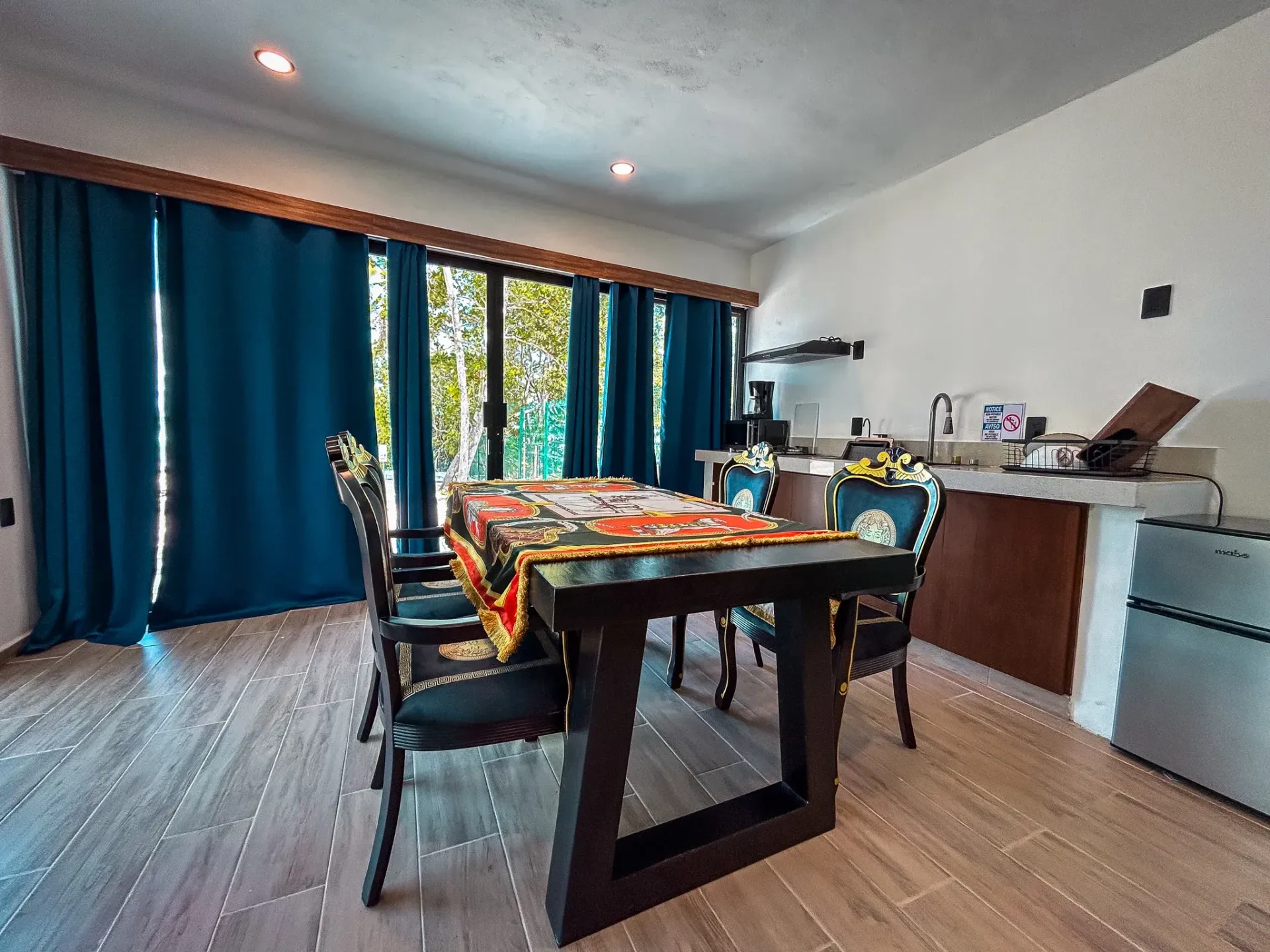Comedor con mesa de madera oscura, sillas estampadas, cortinas azules y puerta corrediza de vidrio.