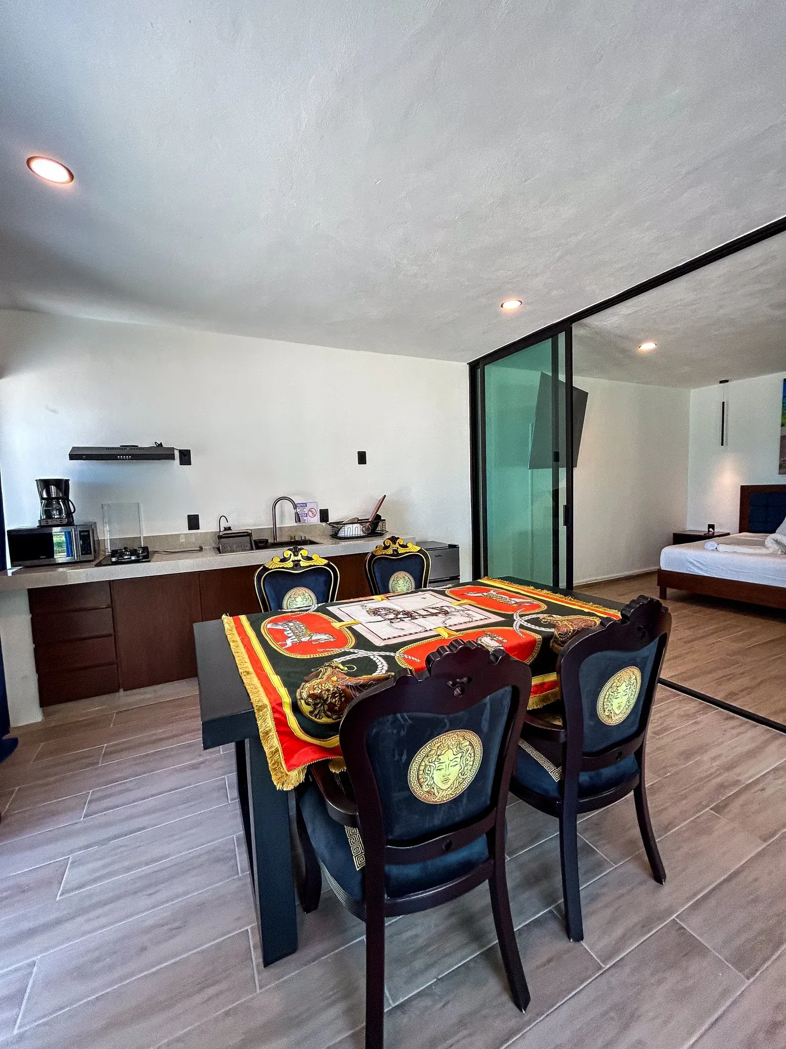 Comedor con mesa negra, sillas Versace y cocina americana. Dormitorio al fondo.