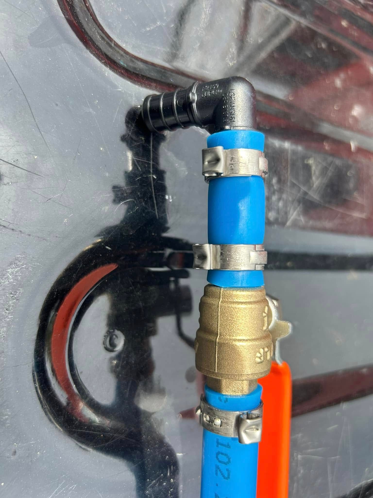Blue and orange pipes with a brass valve and black elbow fitting secured by clamps.