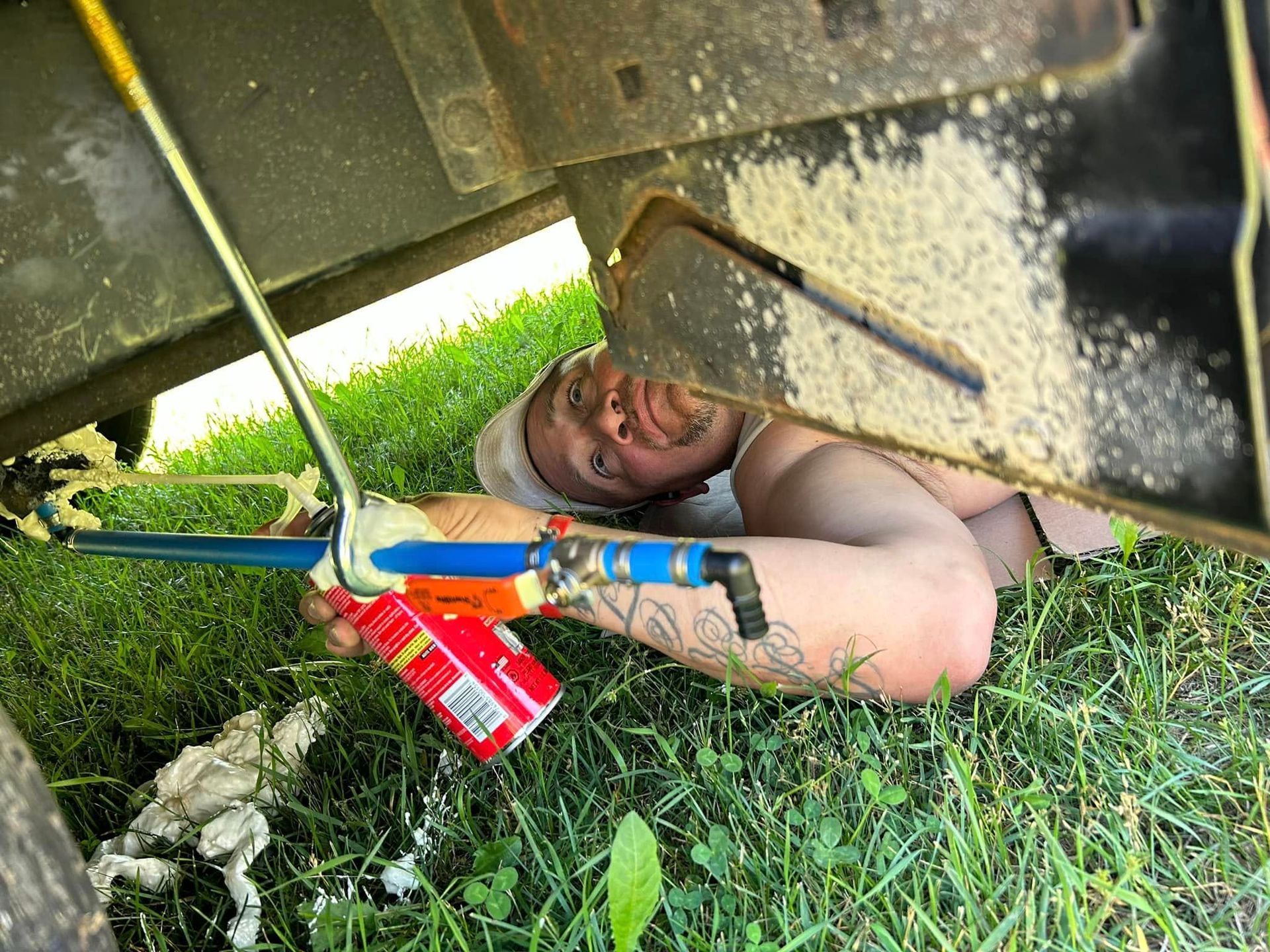 Person working under a vehicle, using a tool. Outdoors on grass.
