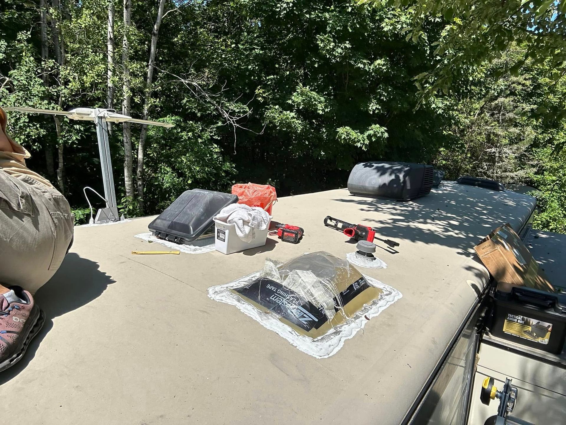 RV roof with vent, tools, and covers. Trees in background.