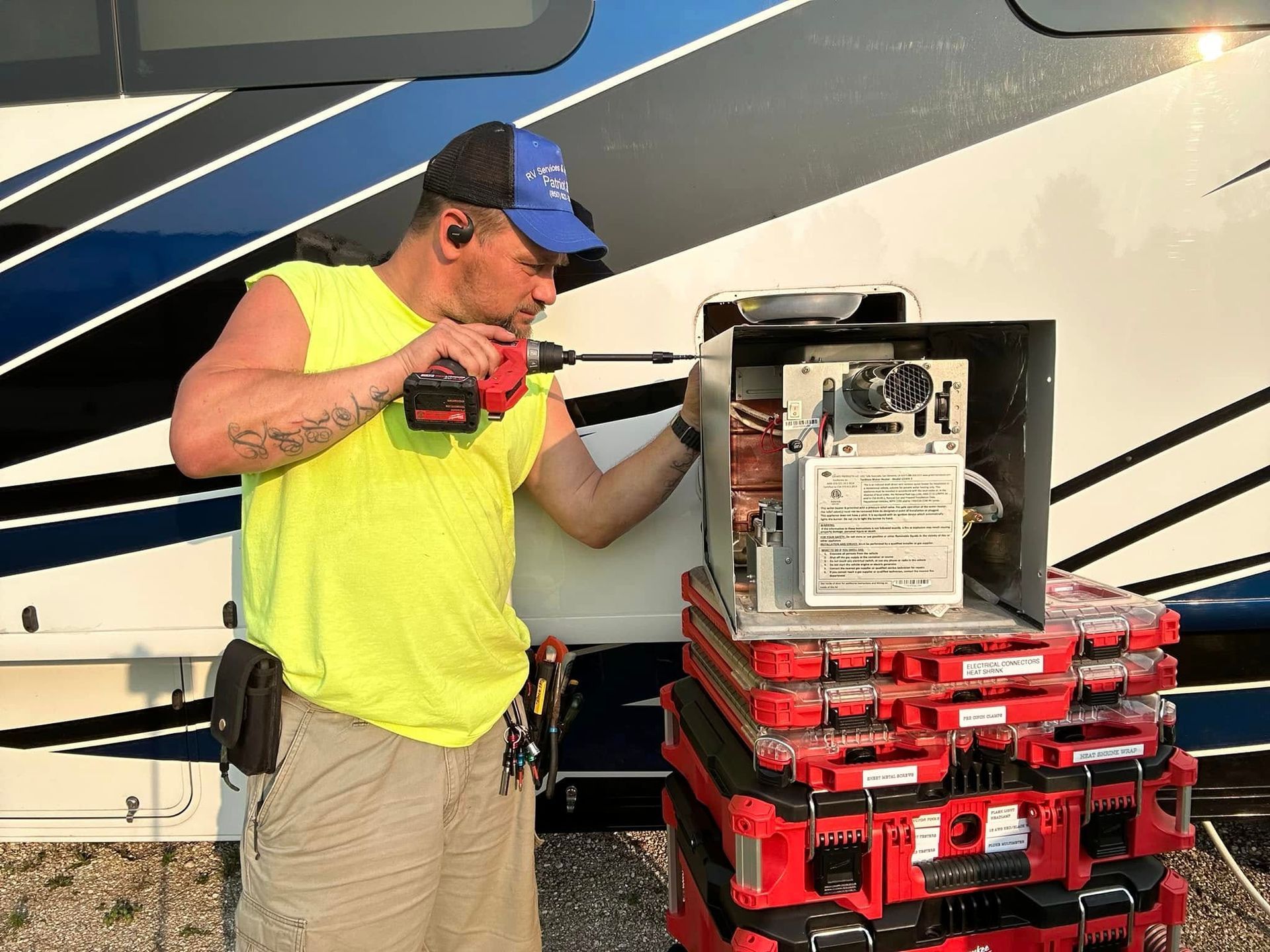 Man in neon shirt using a drill on RV component; tools stacked nearby.