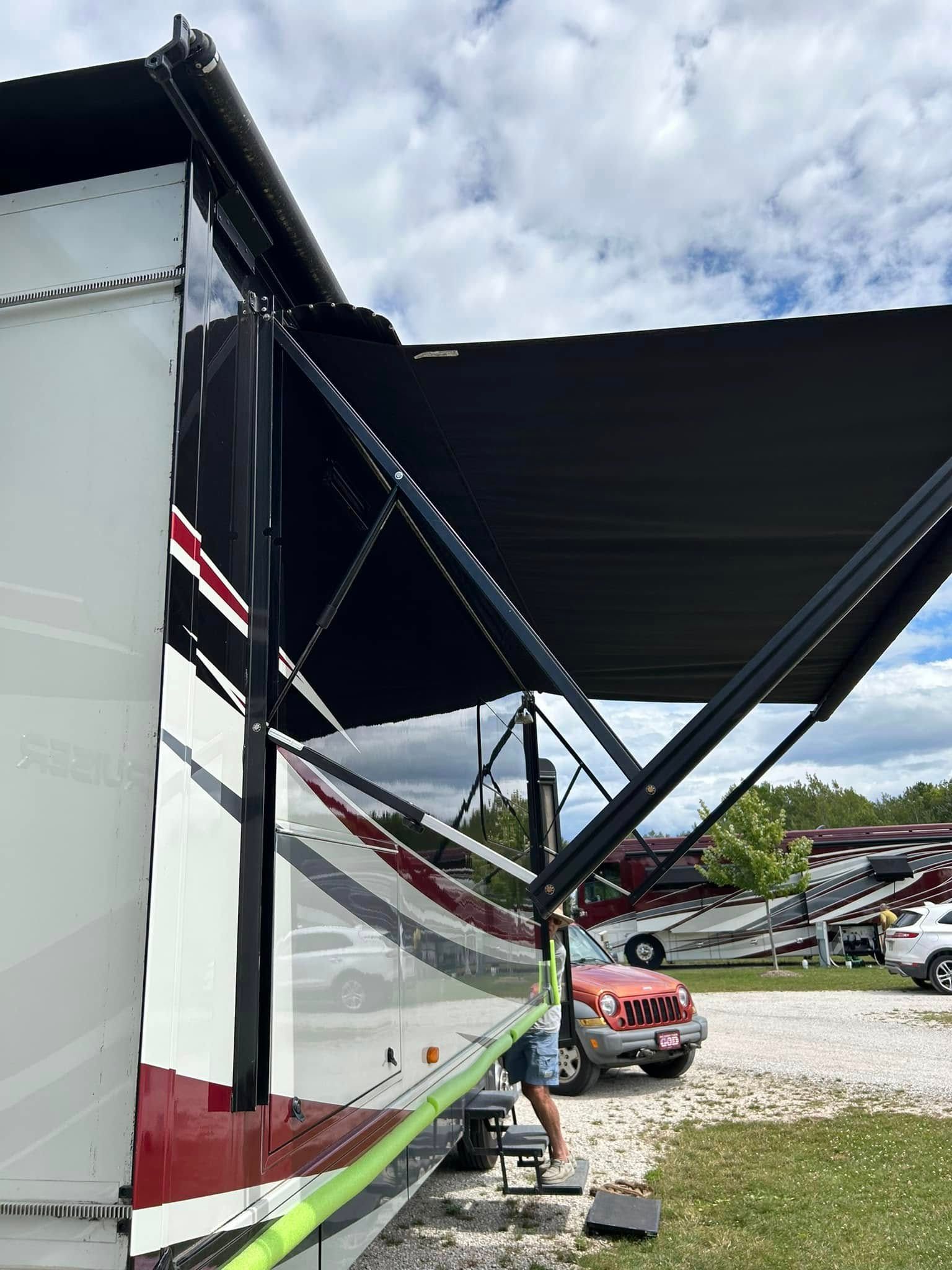 RV with extended black awning and a person on steps; camping setting.