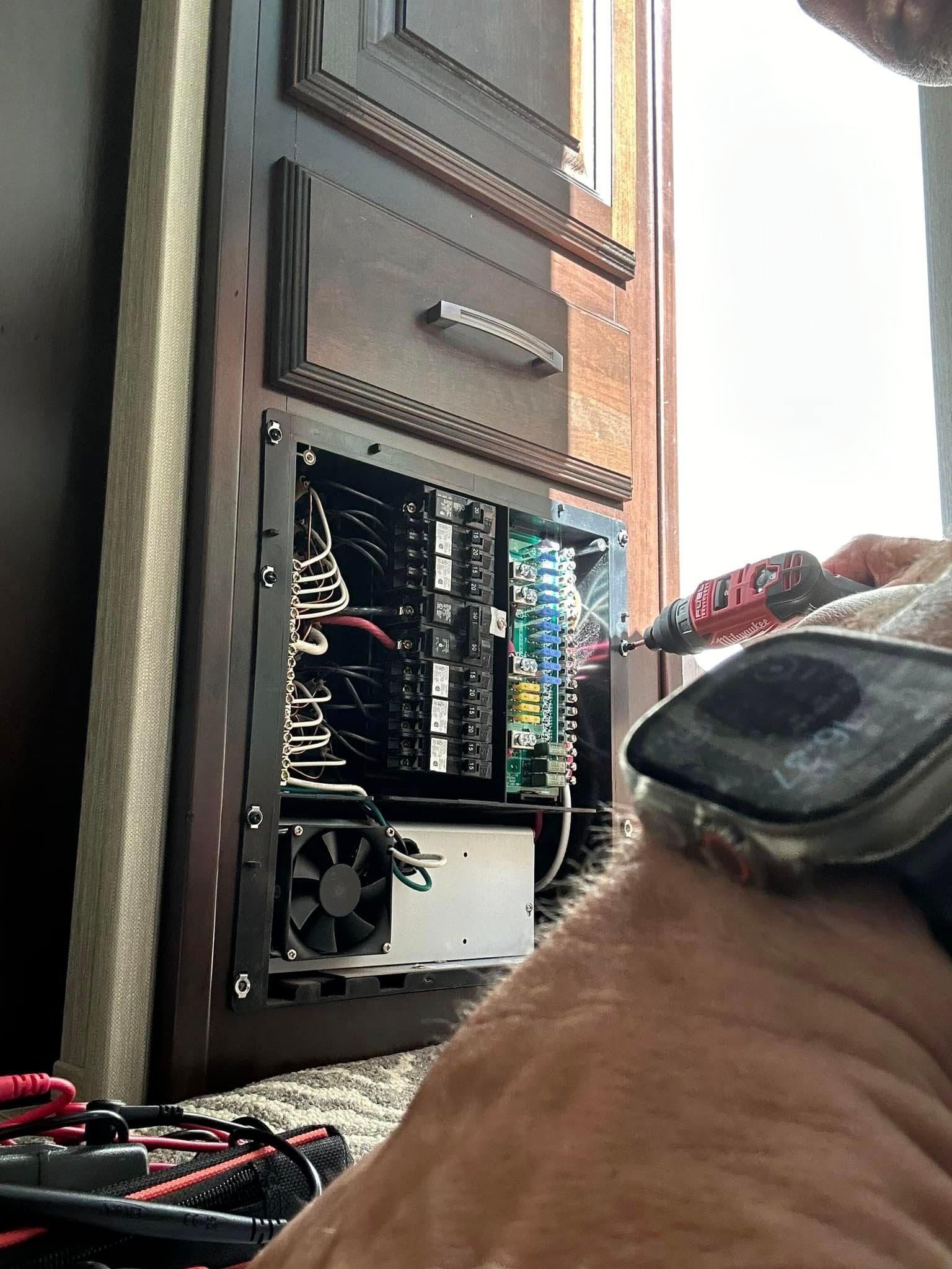 Person working on an RV electrical panel, using a screwdriver. Panel is open, revealing wiring and components.