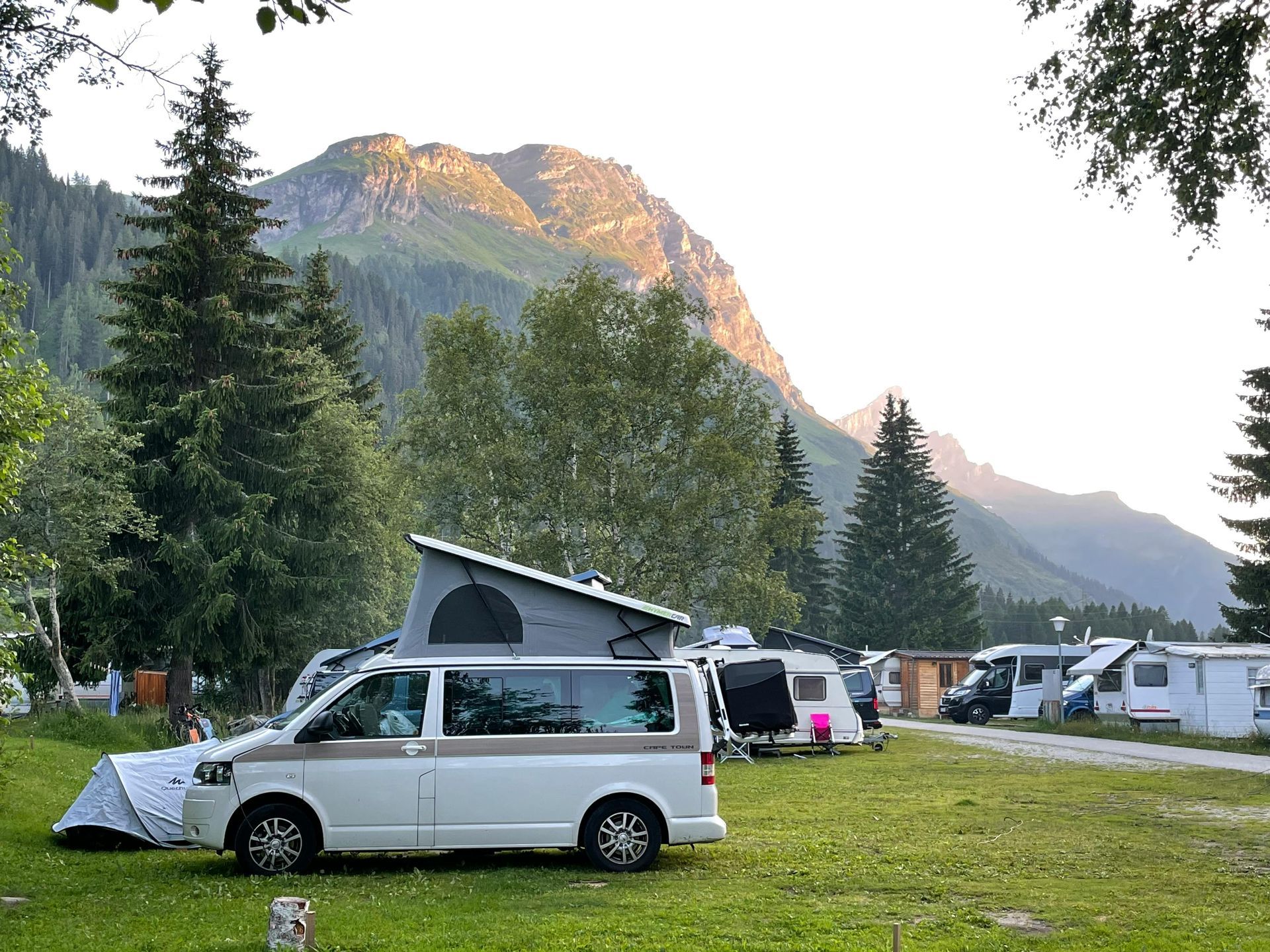 Campsite with RVs and tents set against a mountain backdrop under a sunset sky.