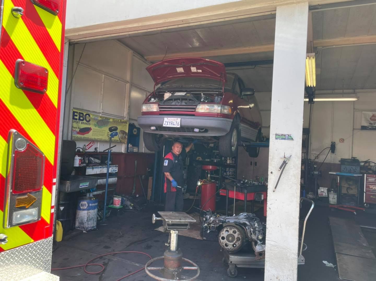 A man is working on a car in a garage next to a fire truck.