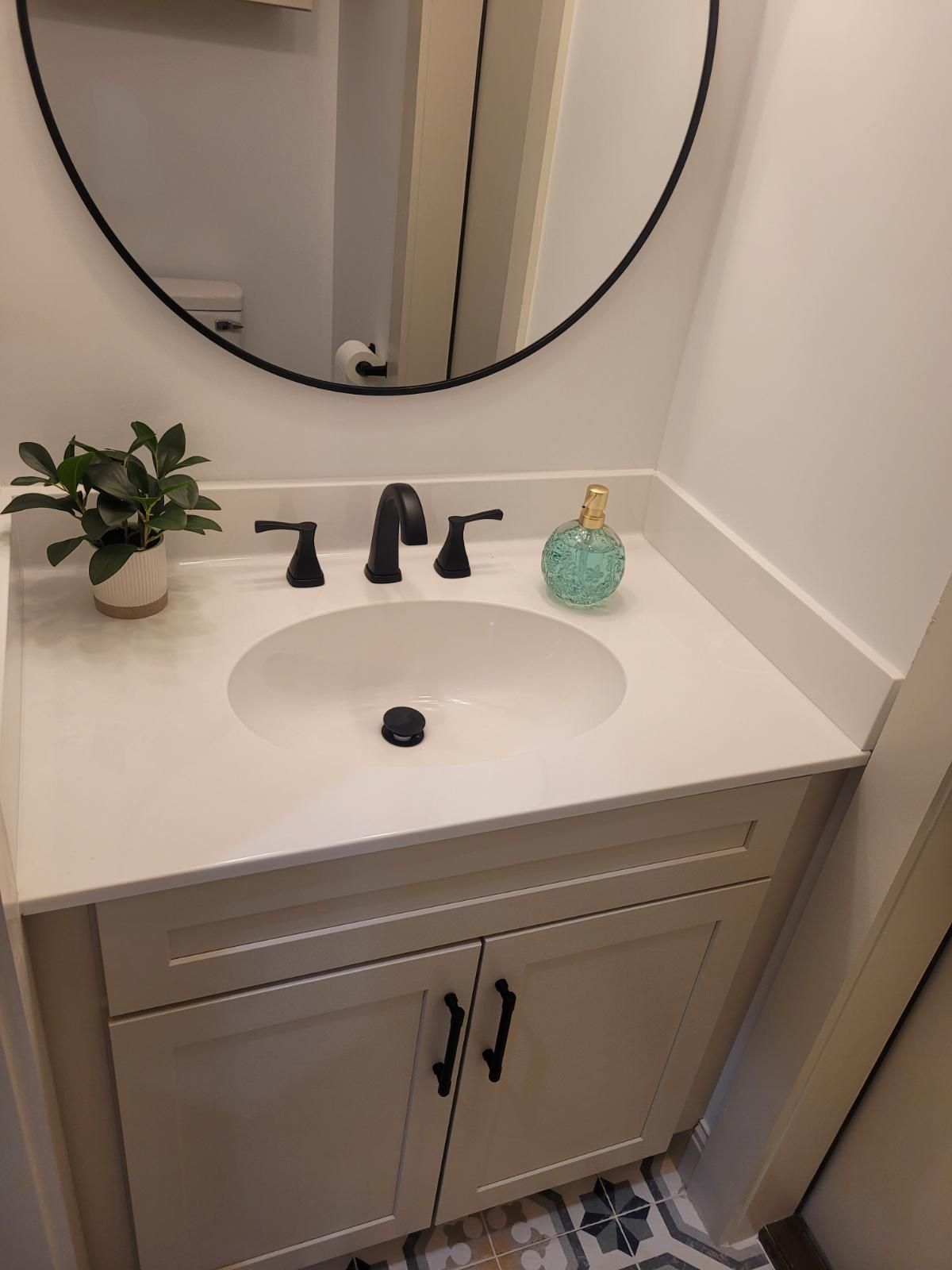 A bathroom sink with a round mirror and a plant on top of it.